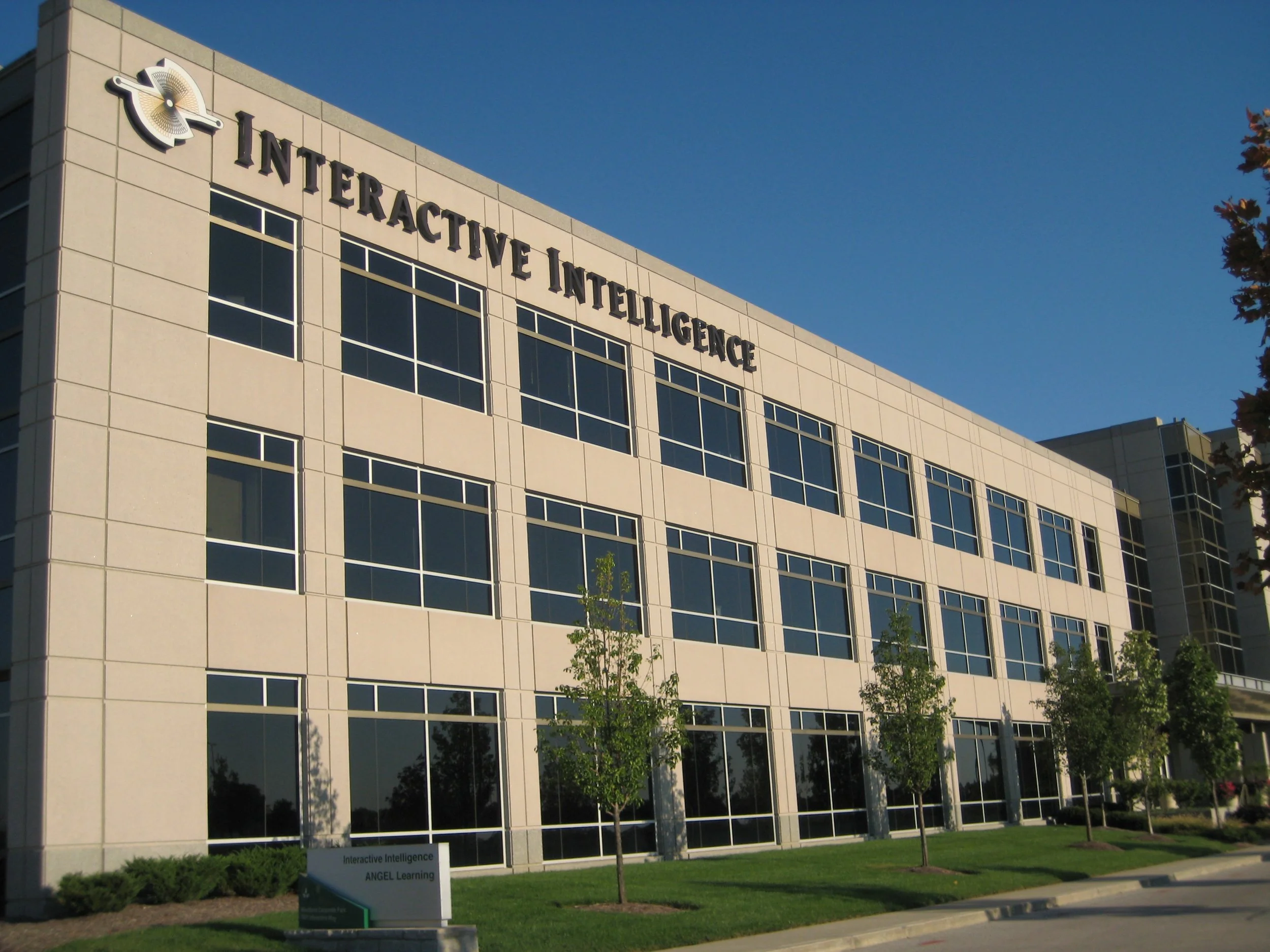 Modern multi-story office building with large windows and the text 'Interactive Intelligence' on the upper part of the facade.