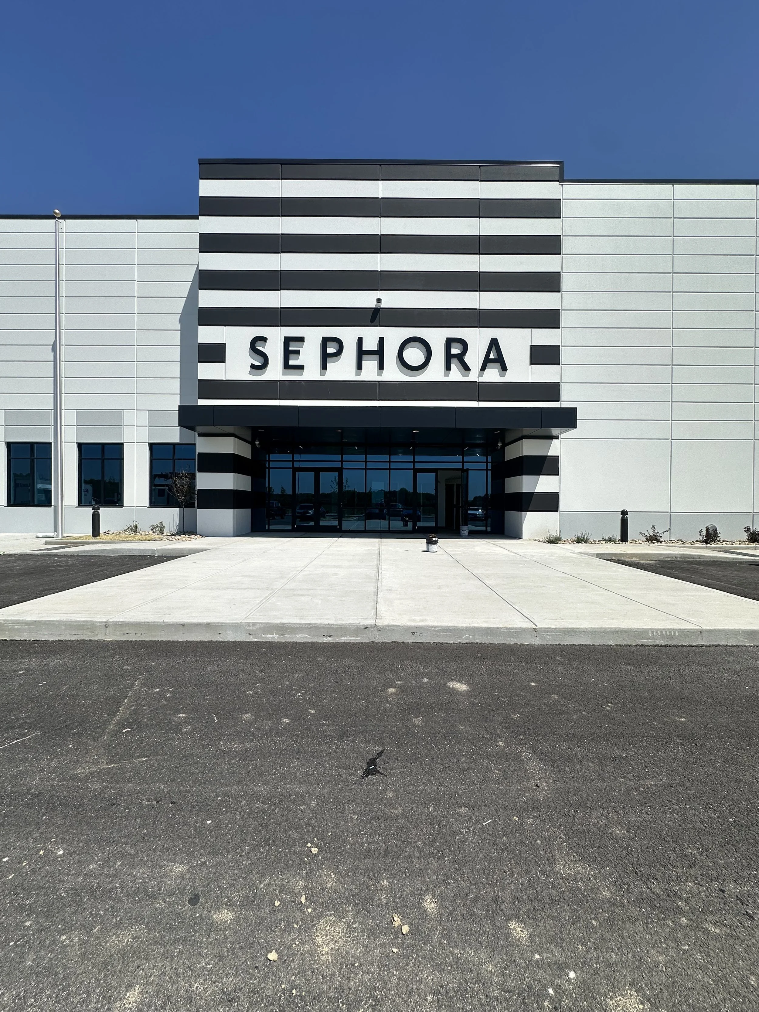 Front view of a modern Sephora store building with black and white horizontal stripes, large glass doors, and clear blue sky.