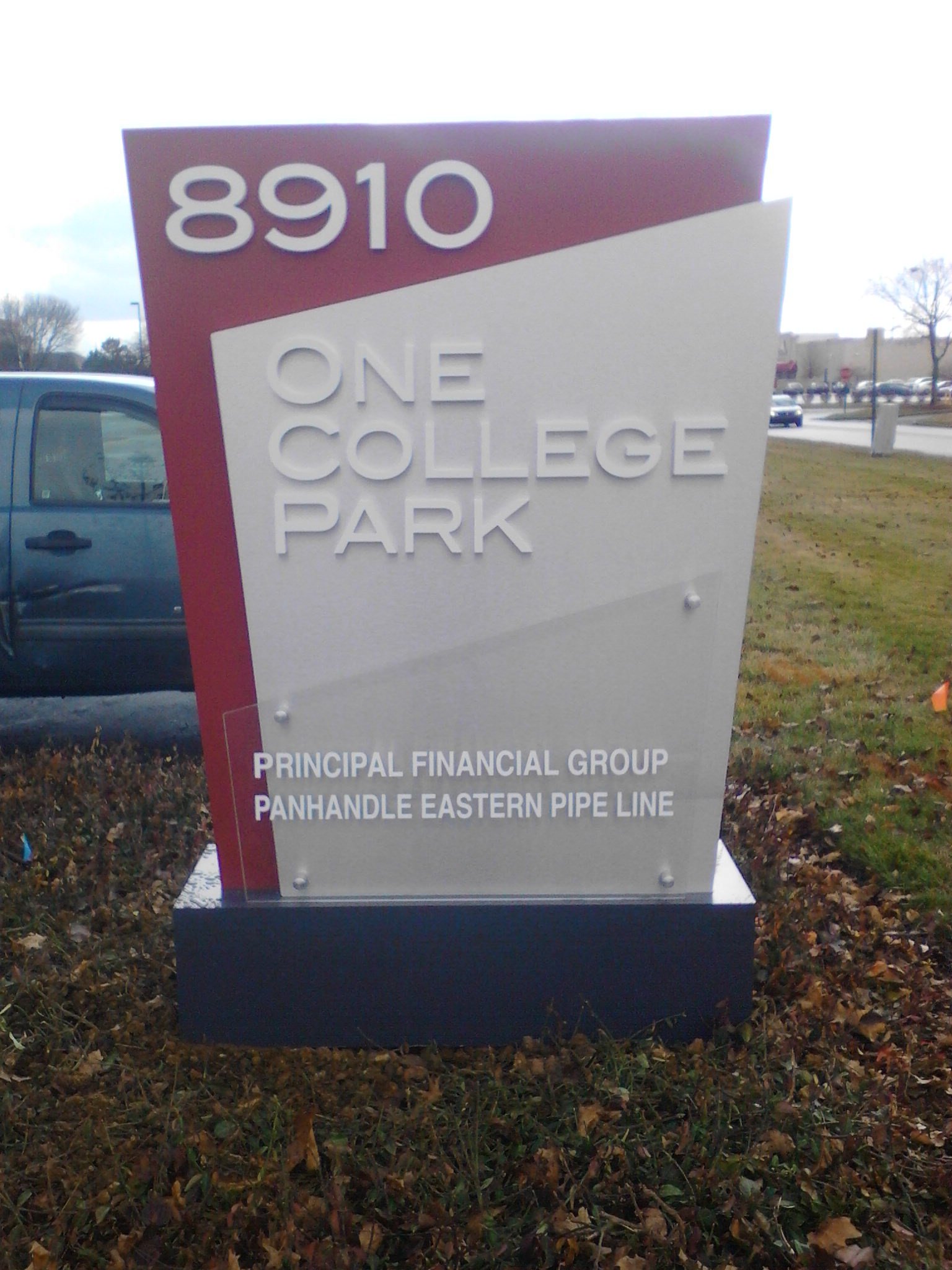 Sign for One College Park with address 8910, and text indicating it is part of Principal Financial Group and Panhandle Eastern Pipe Line, located outdoors near a parking lot and grassy area.