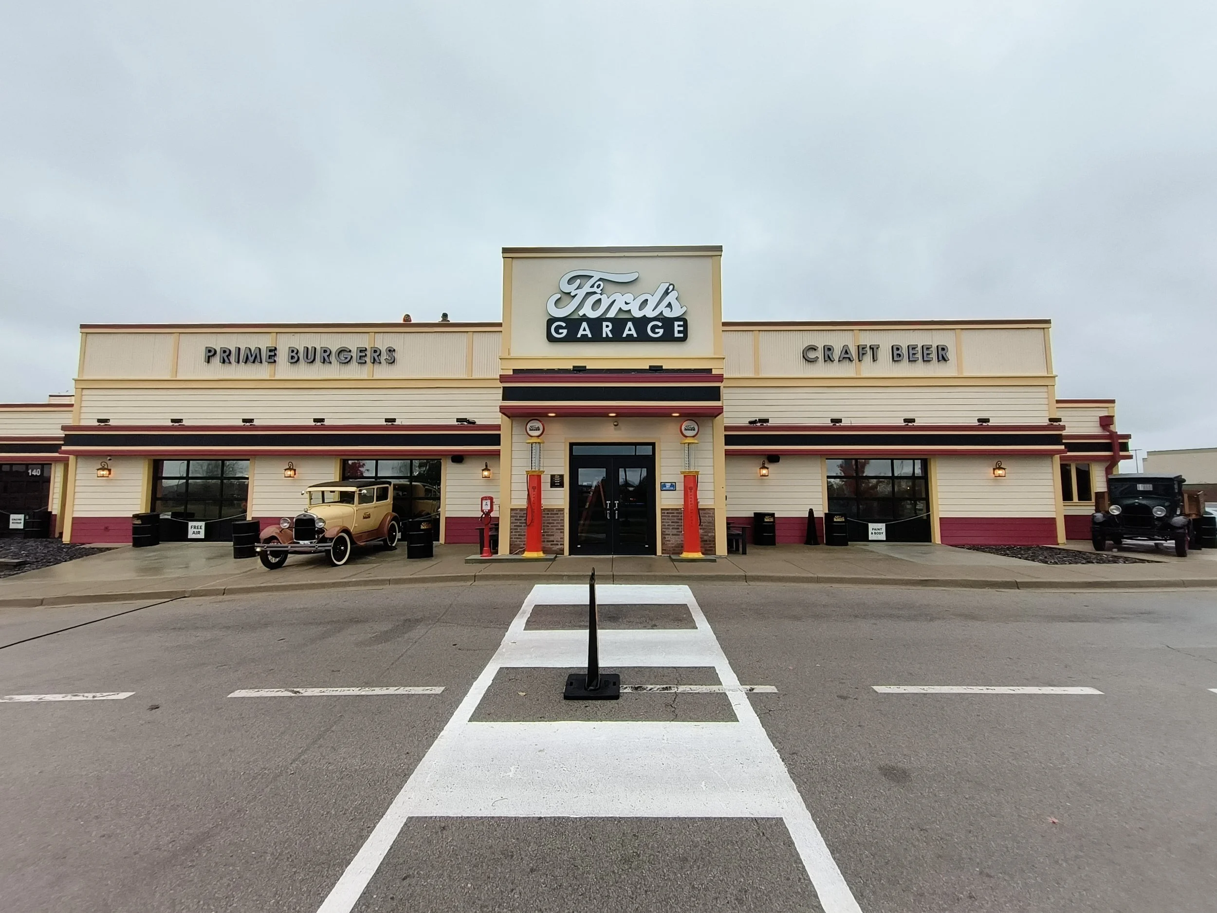 Front view of Ford's Garage restaurant with vintage cars outside, on a cloudy day, featuring signs for prime burgers, craft beer, and Ford's Garage logo.