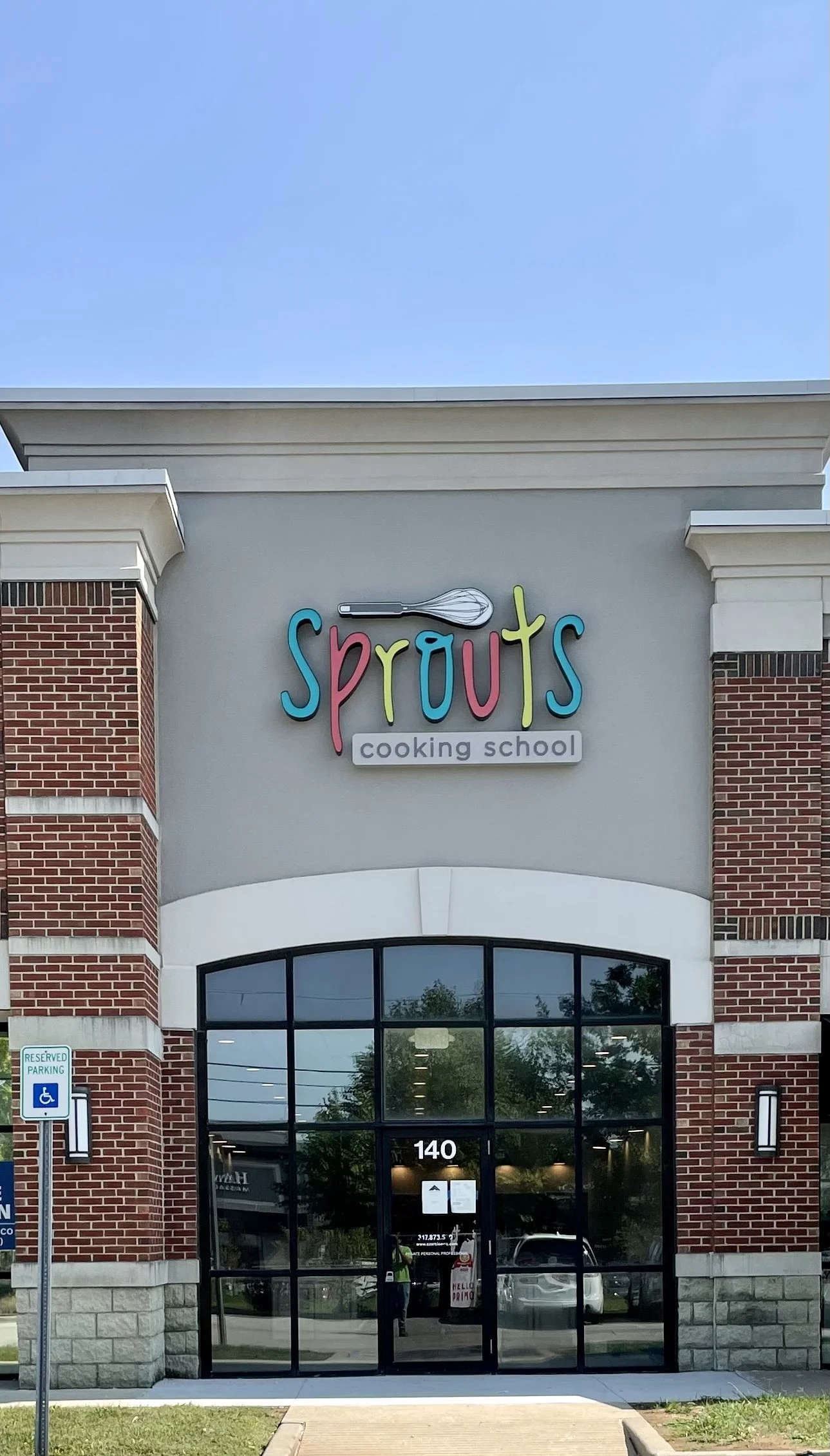 Front of a building with a sign that reads 'Sprouts cooking school' featuring colorful letters and a whisk graphic.