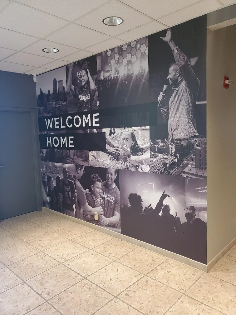 A wall decoration with a collage of black-and-white photos of people at a concert or event, with the words "WELCOME HOME" in bold white letters across the center.