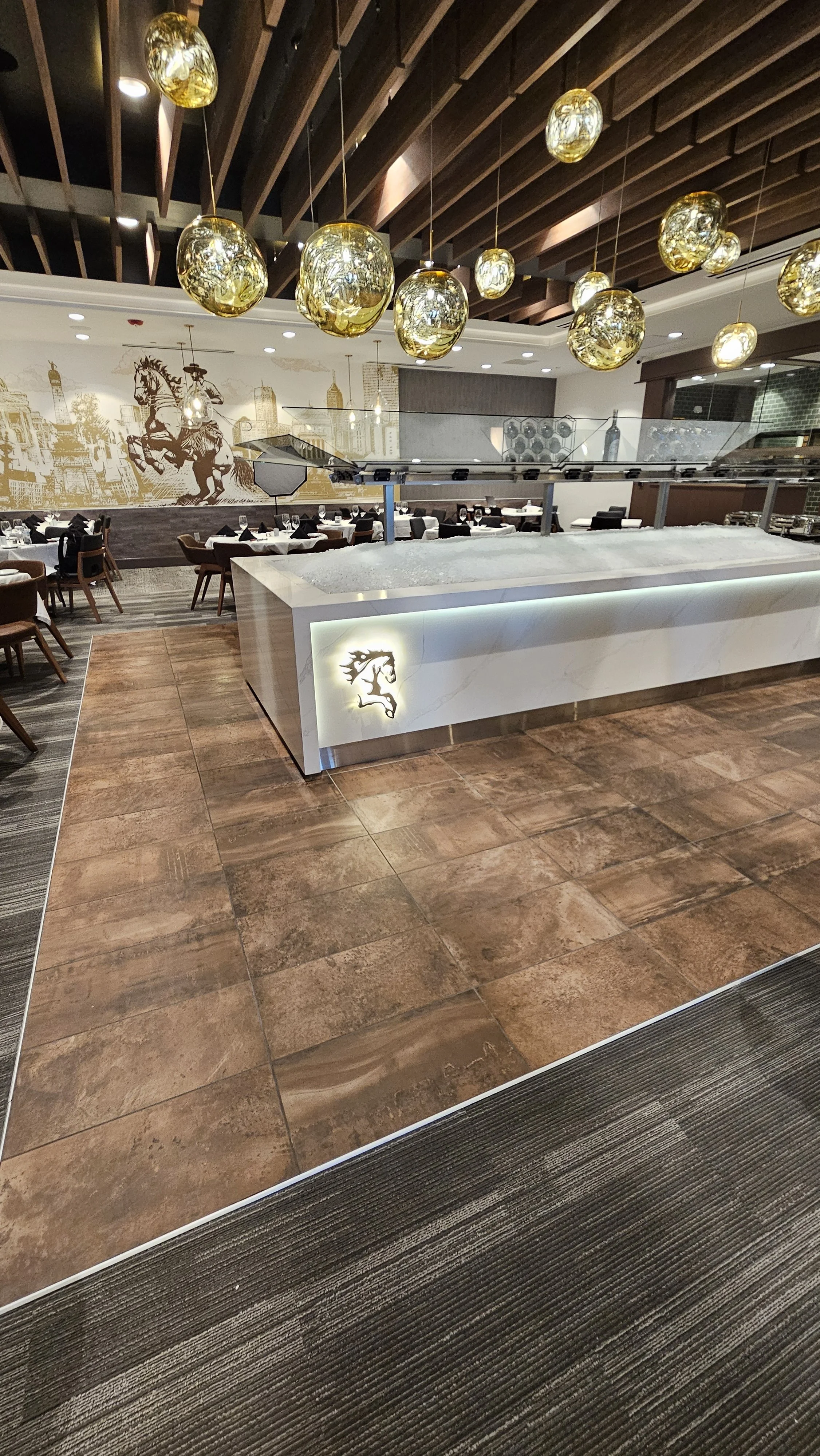 Modern restaurant interior with a white marble buffet counter, decorative hanging gold orbs, and a wall mural of a mounted knight on horseback in the background.