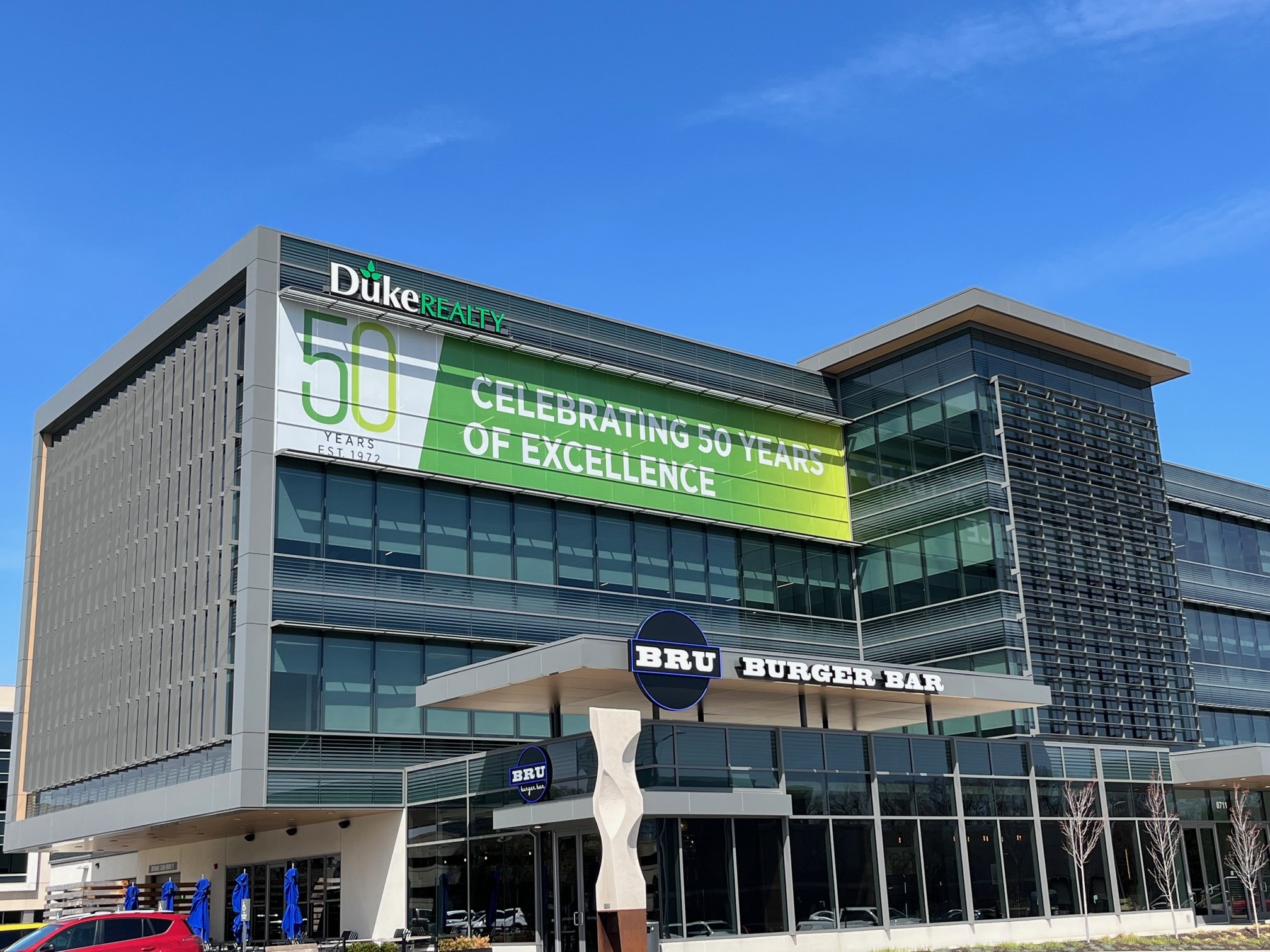 Modern building with a large green banner celebrating 50 years of excellence. The building has glass windows and a sign for BRU Burger Bar on the front.