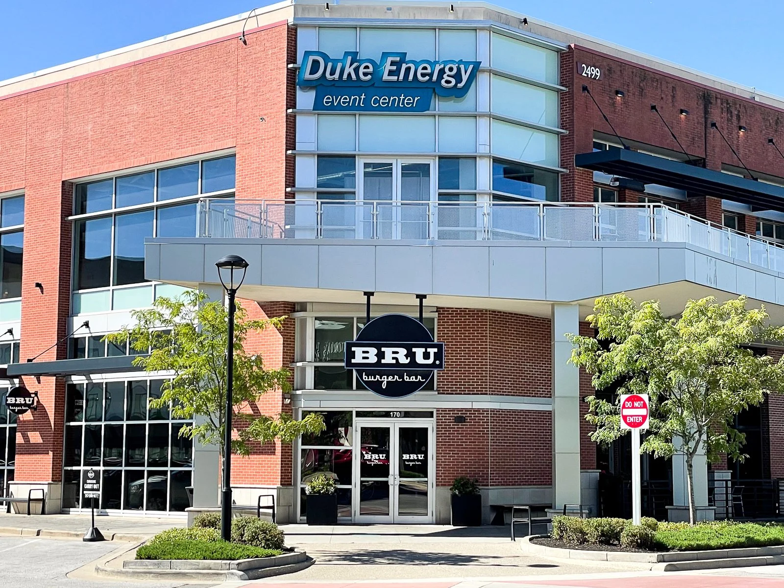 Exterior view of the Duke Energy event center building with a BRU burger bar entrance, trees, street signs, and street lamps.