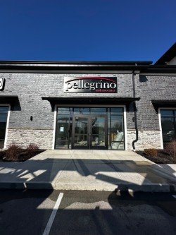 The exterior of a building with a sign that says 'belgrino', a glass entrance door, and parking spaces in the foreground.