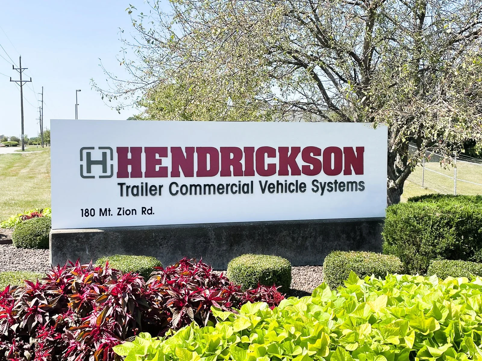 Sign for Hendrickson Trailer Commercial Vehicle Systems at 180 Mt. Zion Rd, surrounded by colorful shrubs and trees in a landscaped area.