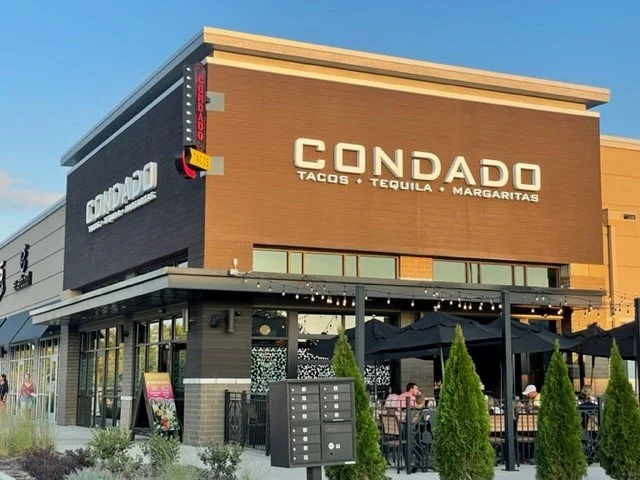 Exterior view of Conado restaurant with outdoor seating, umbrellas, and a sign indicating it serves tacos, tequila, and margaritas.