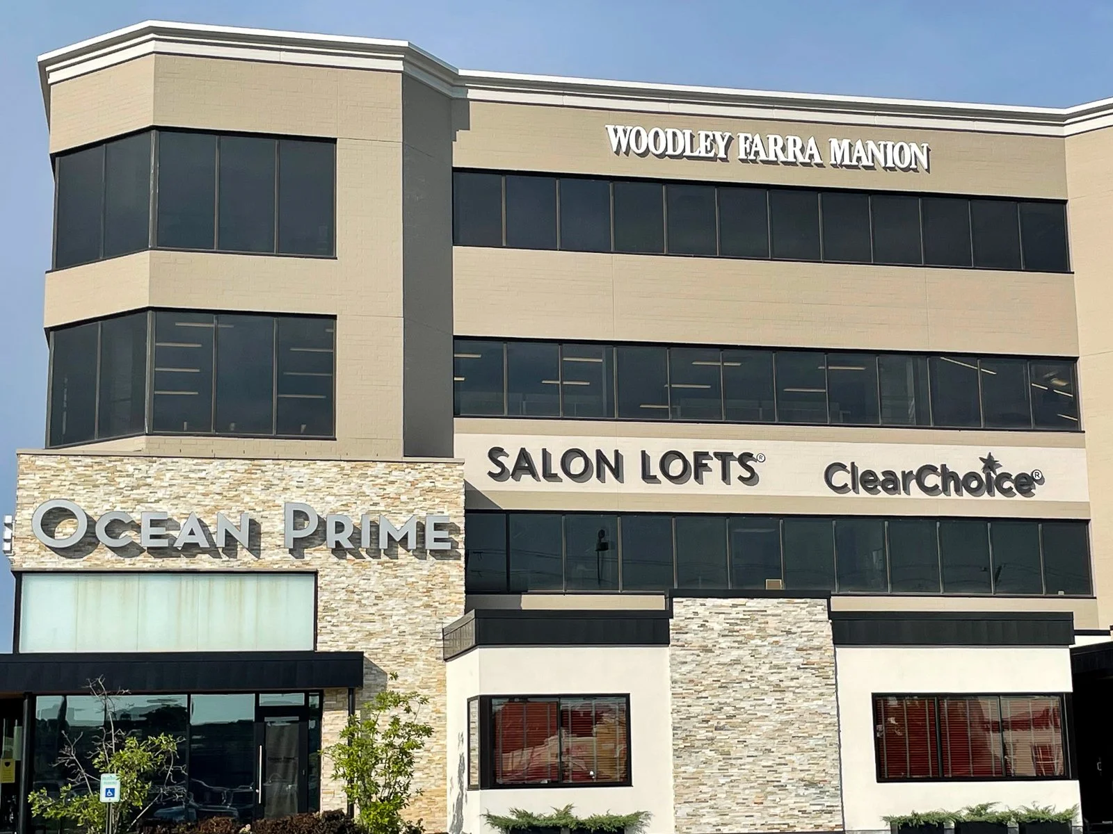 A modern multi-story commercial building with signs for Ocean Prime, Salon Lofts, and ClearChoice, located at Woodley Farrar Marion.