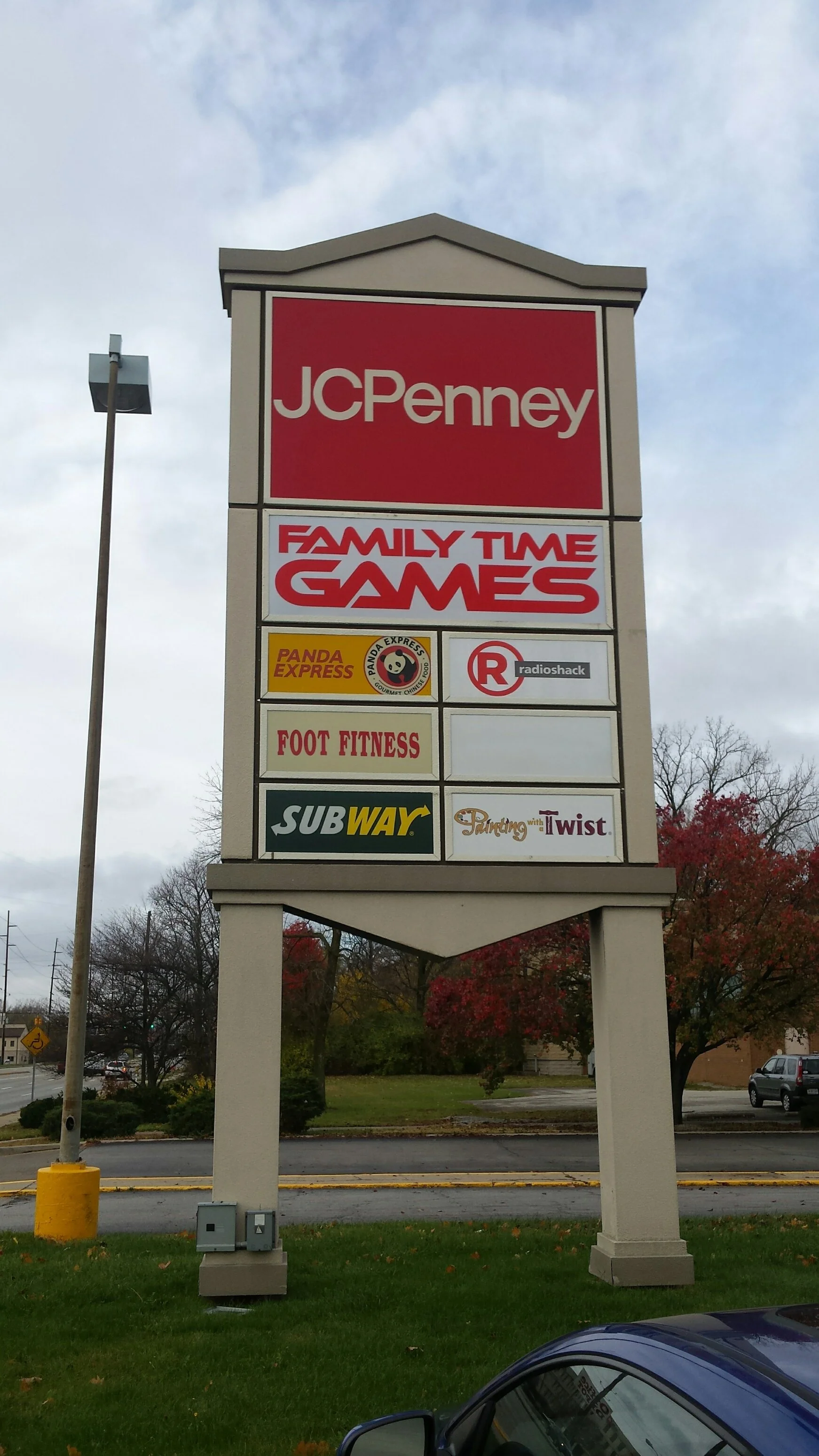 A large outdoor shopping mall sign displaying logos for JCPenney, Family Time Games, Panda Express, RadioShack, Foot Fitness, Subway, and Tanning with a Twist.