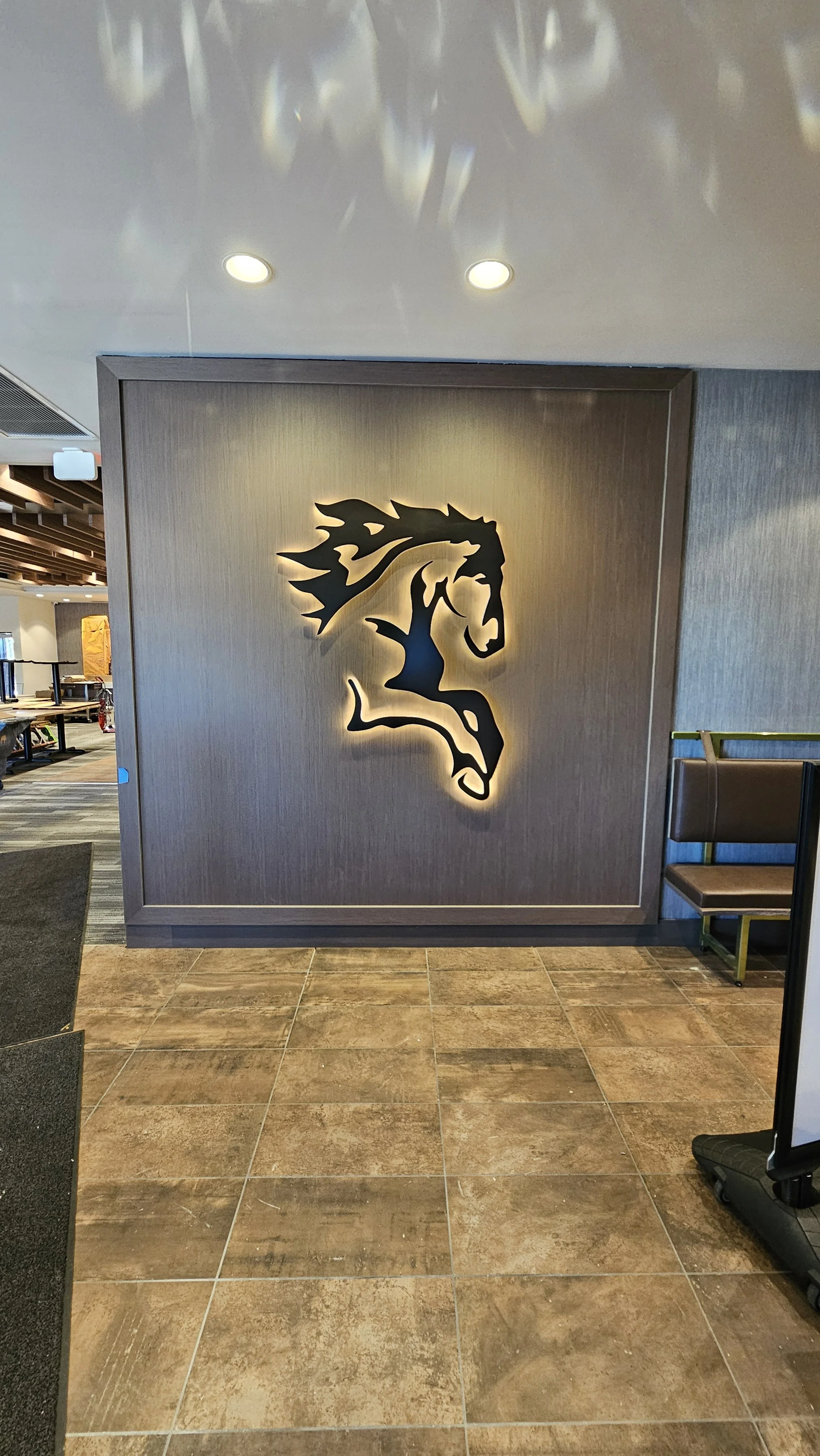A backlit black logo of a horse's head on a wooden wall in an indoor setting.