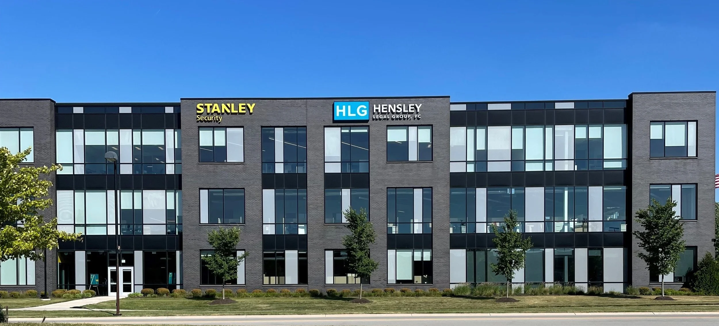 Modern office building with glass windows and a brick facade, featuring signs for Stanley Security and HLG Hensley Legal Group, PC on the top