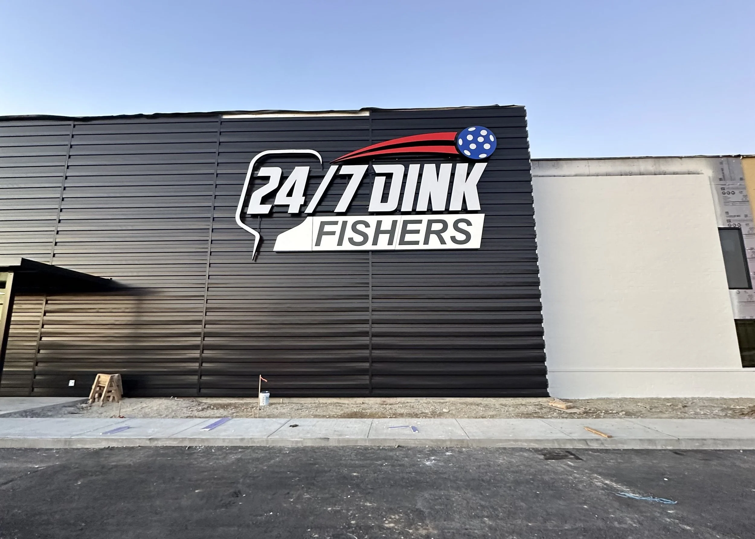 Commercial building with a sign that reads '24/7 DINK FISHERS' and a graphic of a billiard ball with a red trail above the sign.
