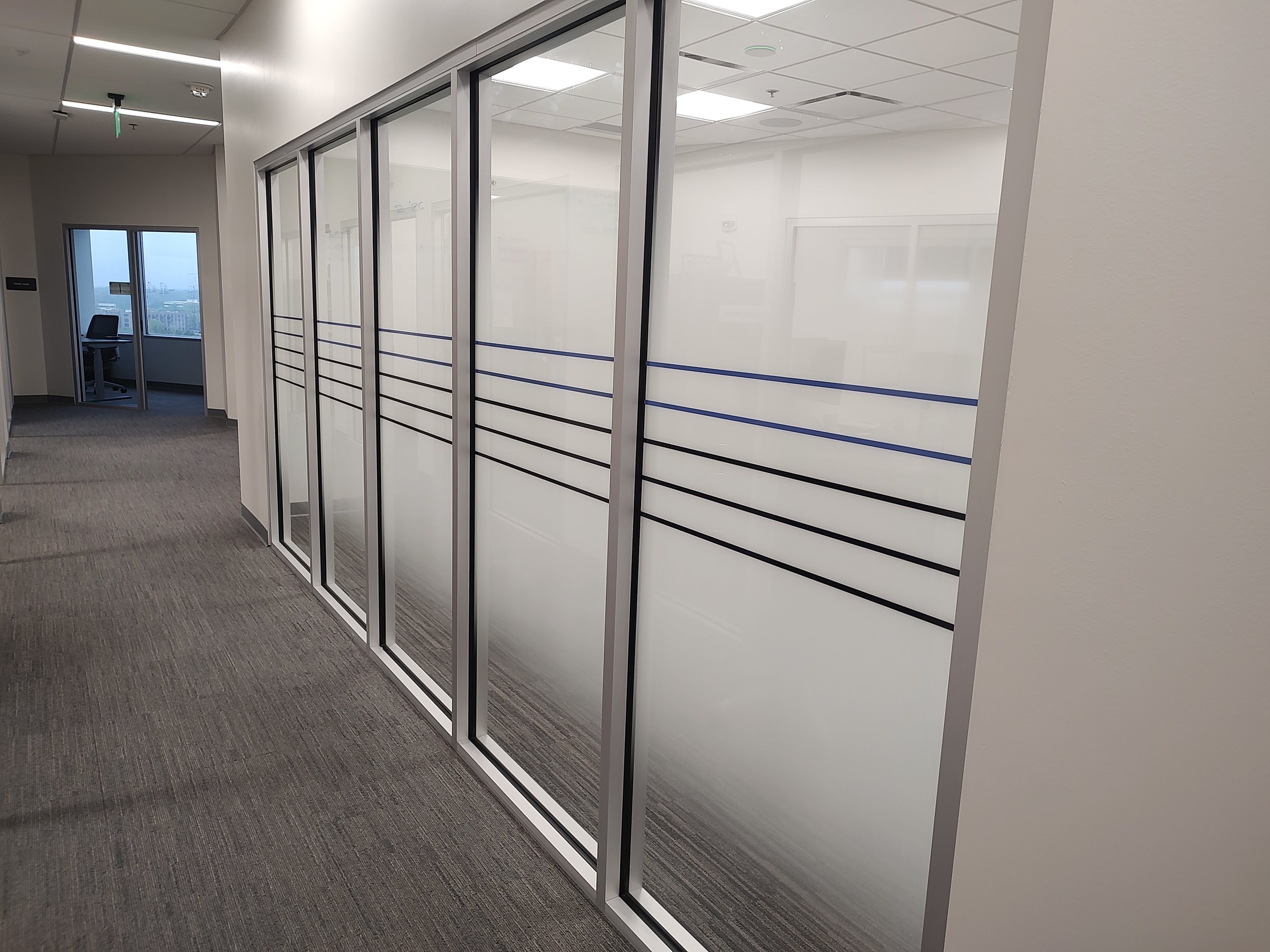 Modern office hallway with glass-walled conference rooms featuring horizontal blue and black stripes.