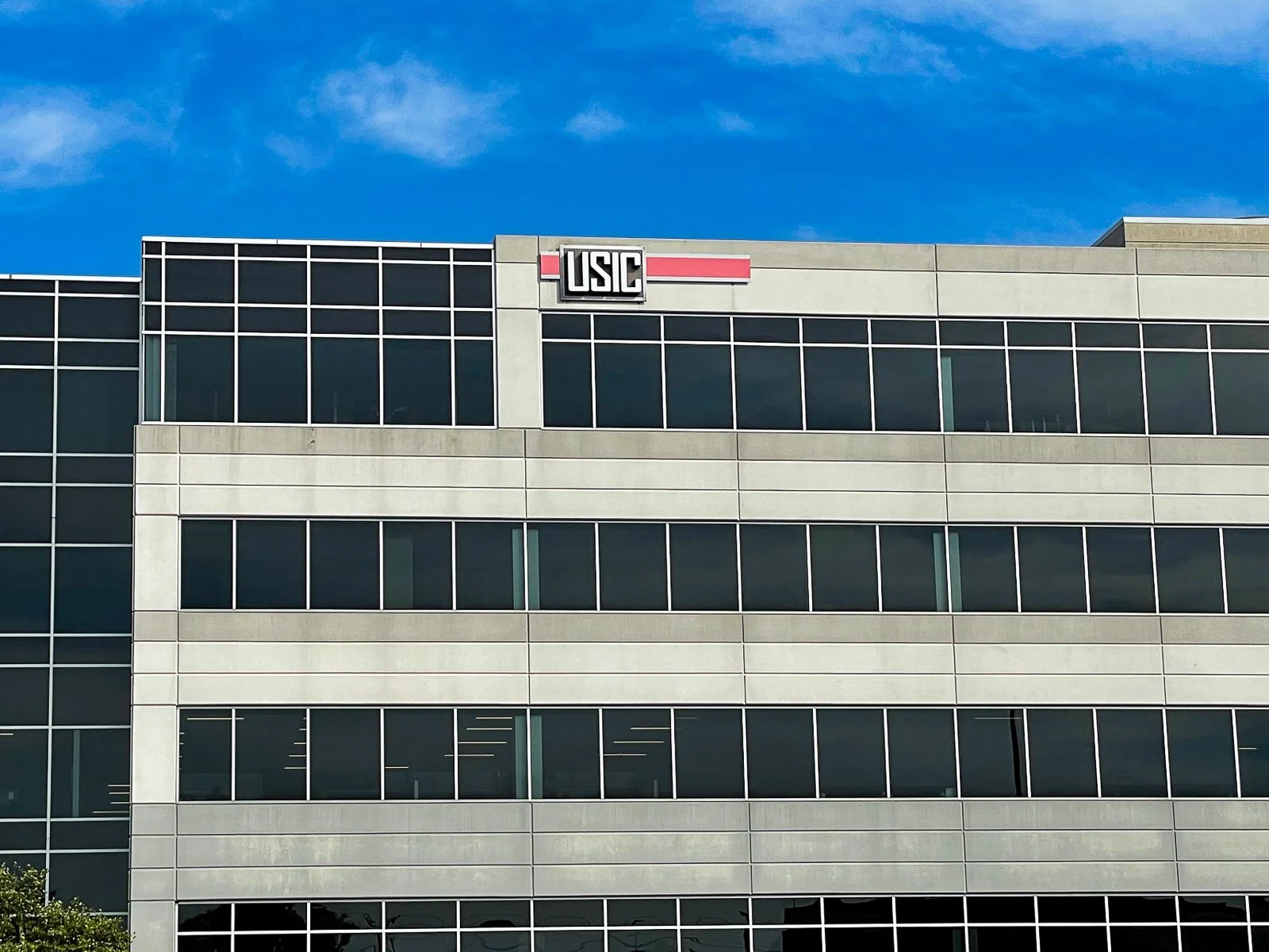 Modern multi-story office building with large glass windows and a sign that reads "USIC" on the top corner.