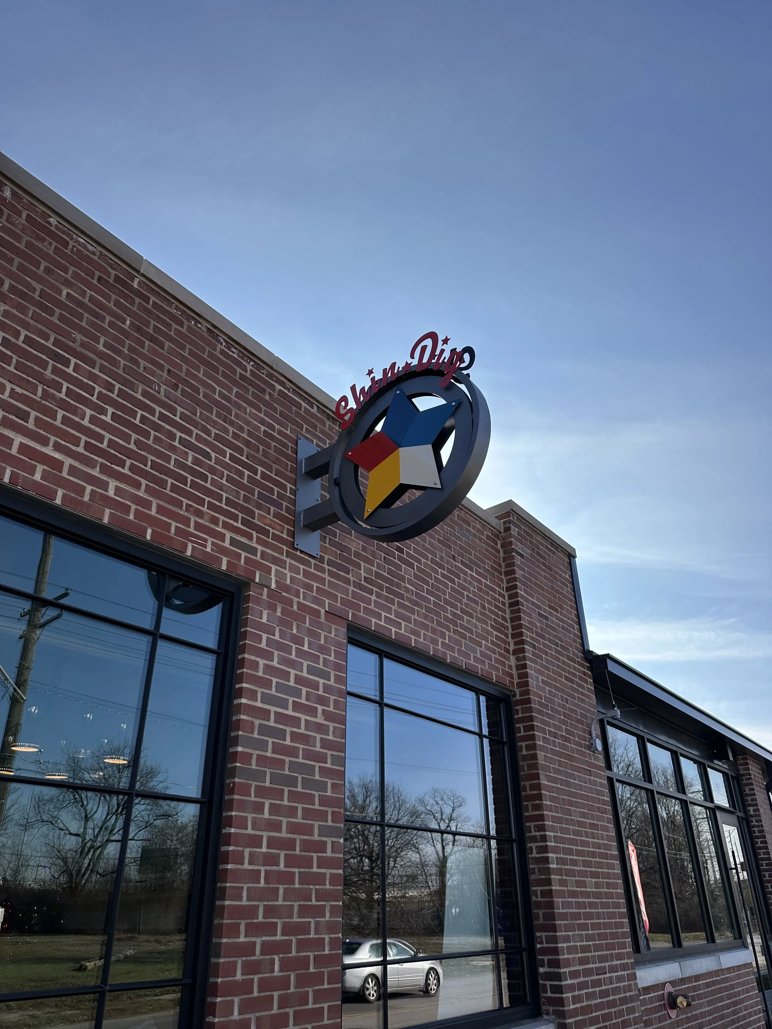 Exterior view of a brick building with large windows and a colorful star logo that says 'Shum Dig' on the side.