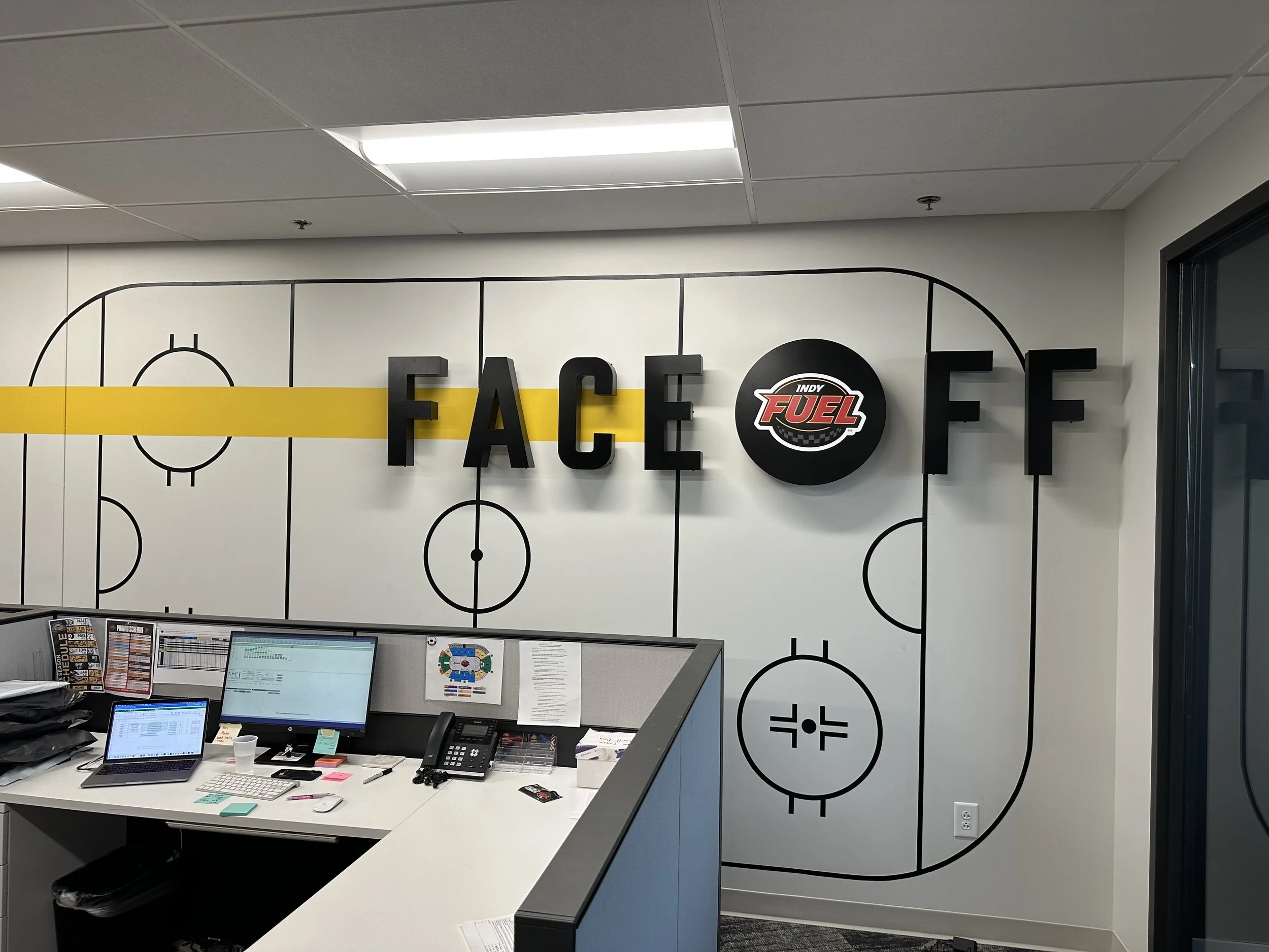 Office wall decorated with a hockey rink outline and the words 'FACE OFF' with the Indy Fuel logo replacing the letter 'O'.