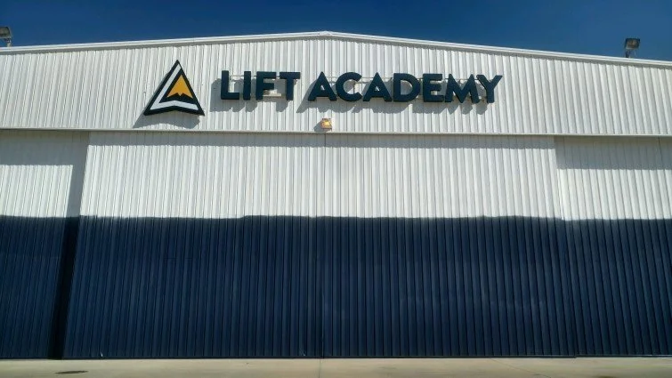 Front view of a white industrial building with a sign that reads 'LIFT ACADEMY' and a logo featuring a mountain peak.