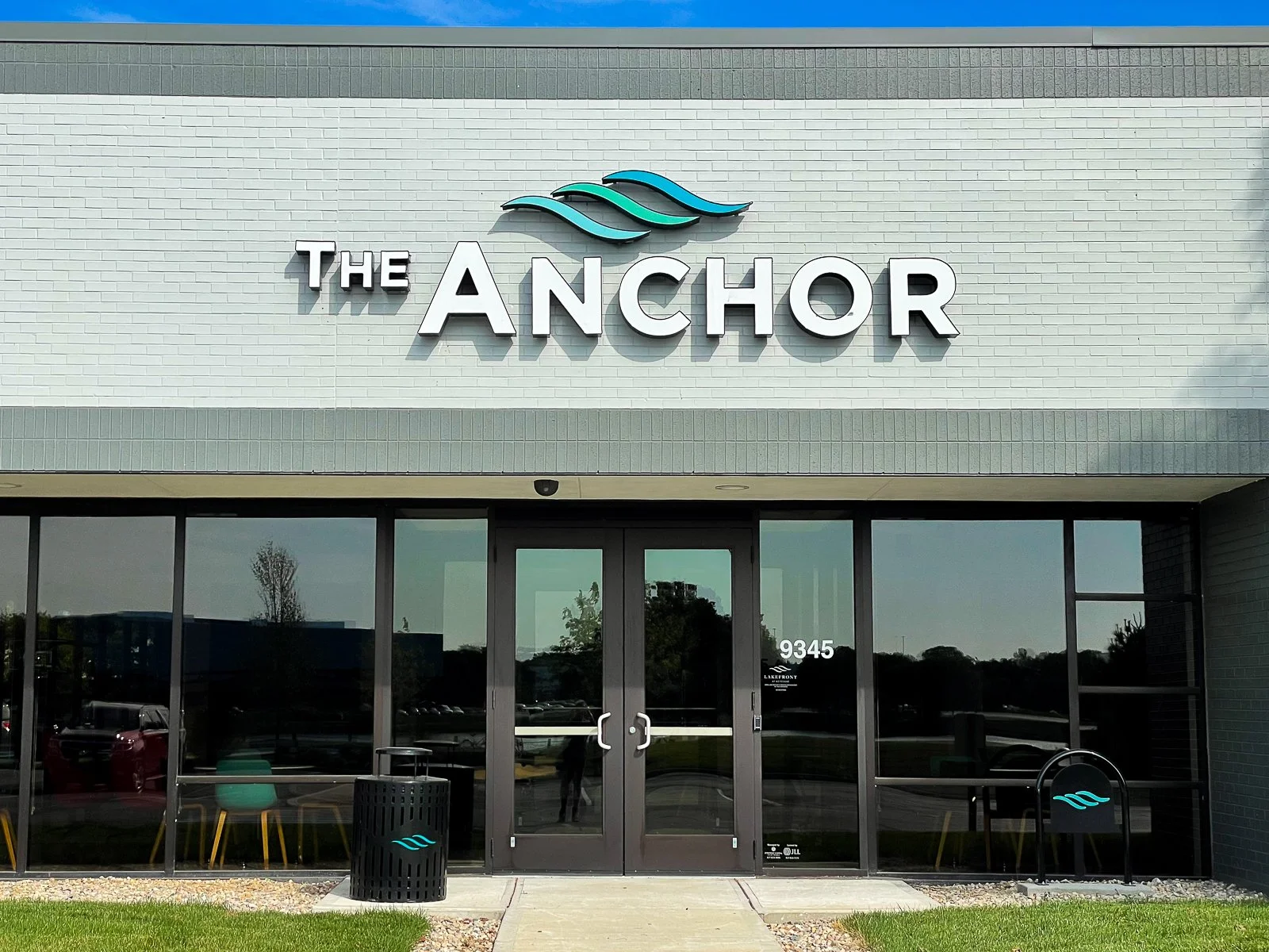 Front of a commercial building with a sign reading 'The Anchor' and a logo of three stylized waves above the name.