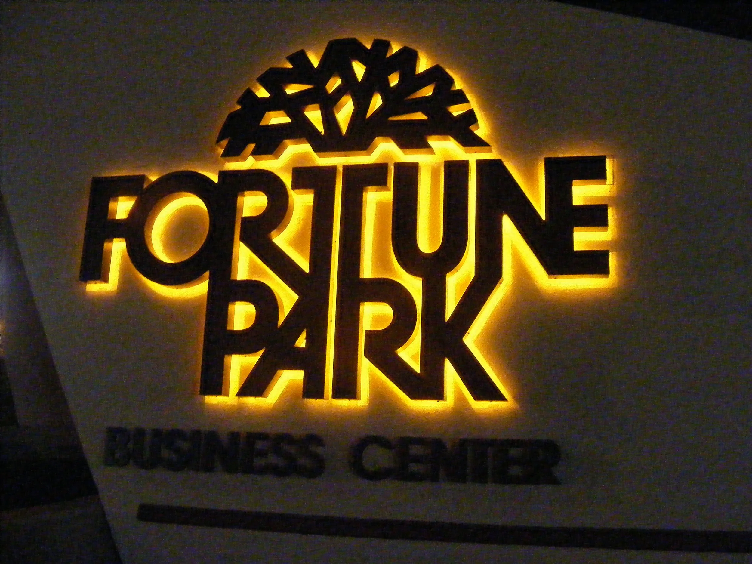 Illuminated sign for Fortune Park Business Center with the words and logo glowing against a wall.