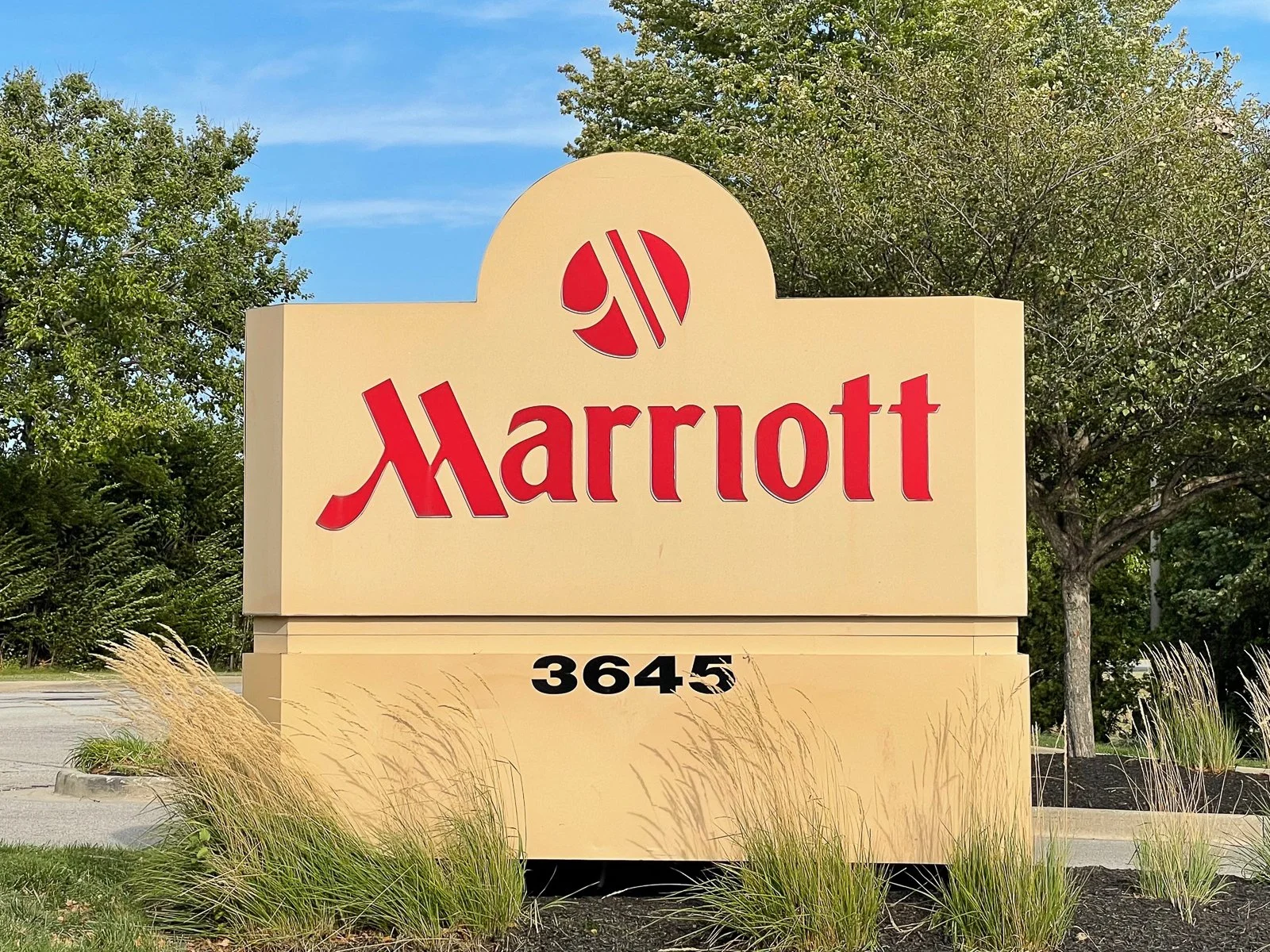 Marriott hotel sign with a beige background, red logo, and black address number 3645, surrounded by grass and trees.
