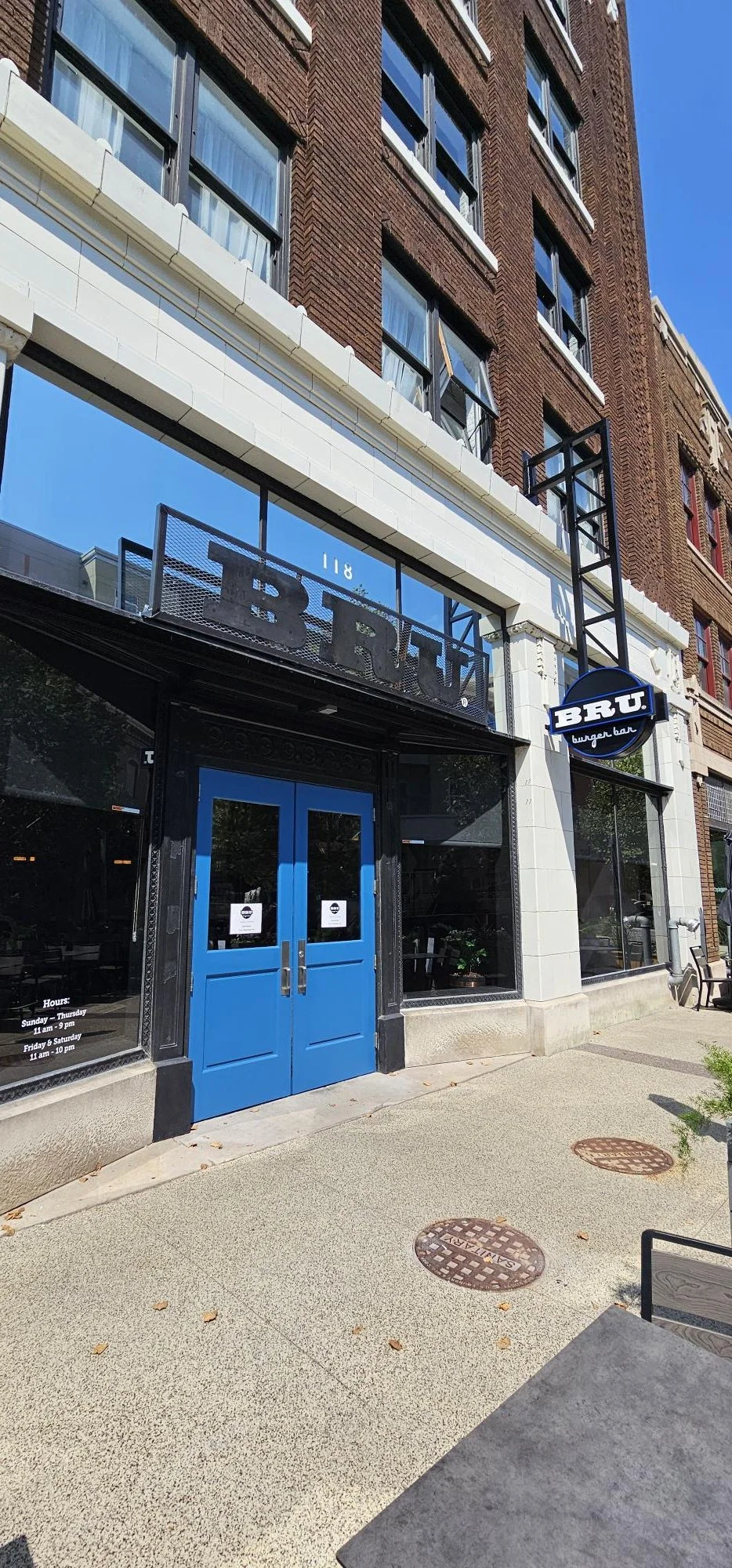 Exterior view of a burger bar named BRUT with a blue double door entrance and black signage, located in an urban area with a brick building facade and sidewalk.