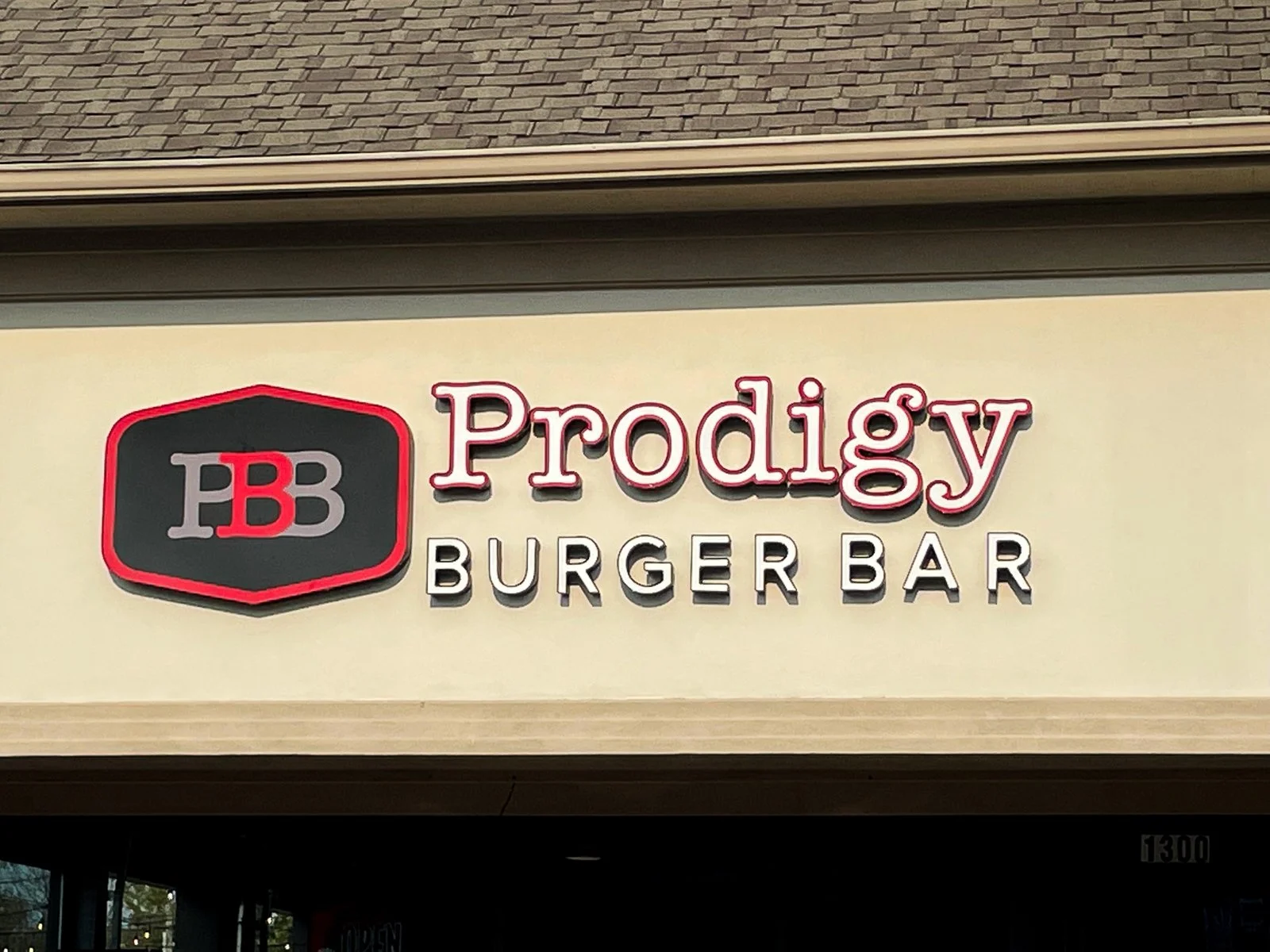 Prodigy Burger Bar sign with logo featuring two red and gray B's inside a black hexagon outline.
