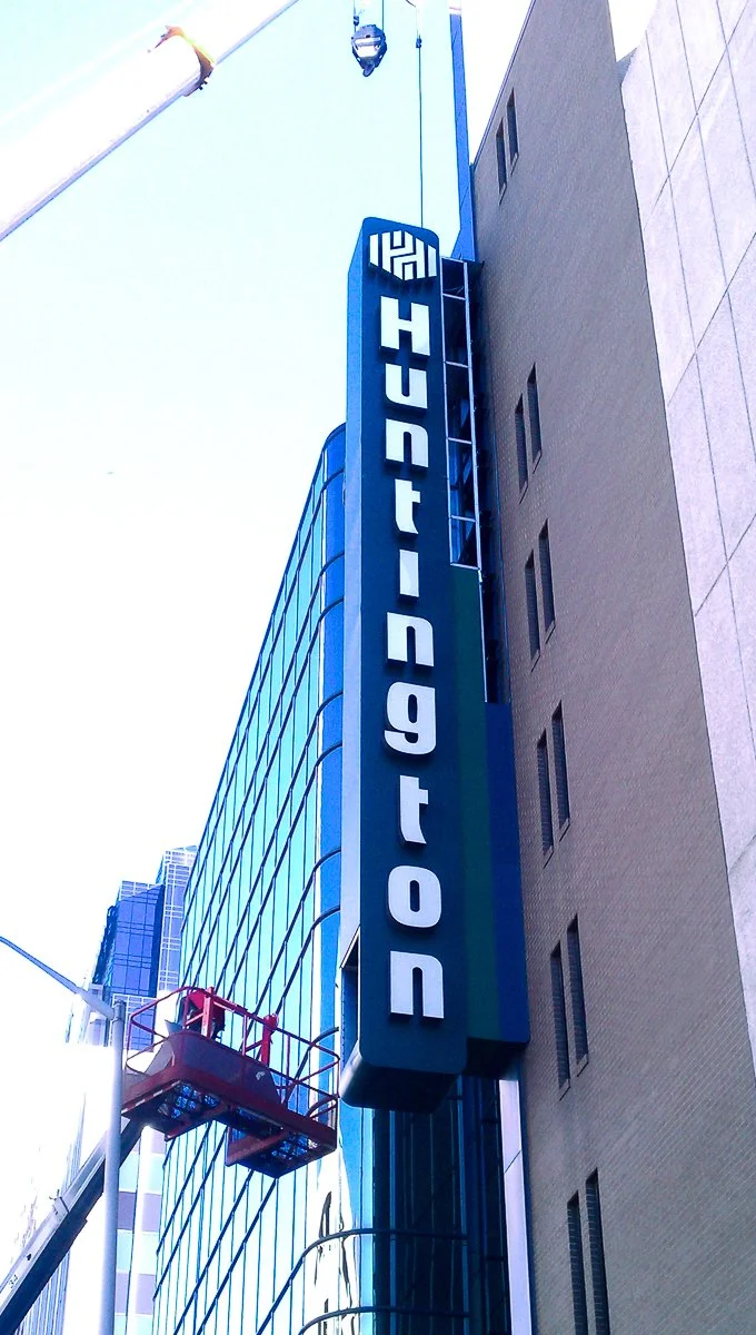 Vertical sign reading 'DID YOU KNOW' on a building in an urban area, with a cherry picker lift nearby, and tall glass skyscrapers in the background.