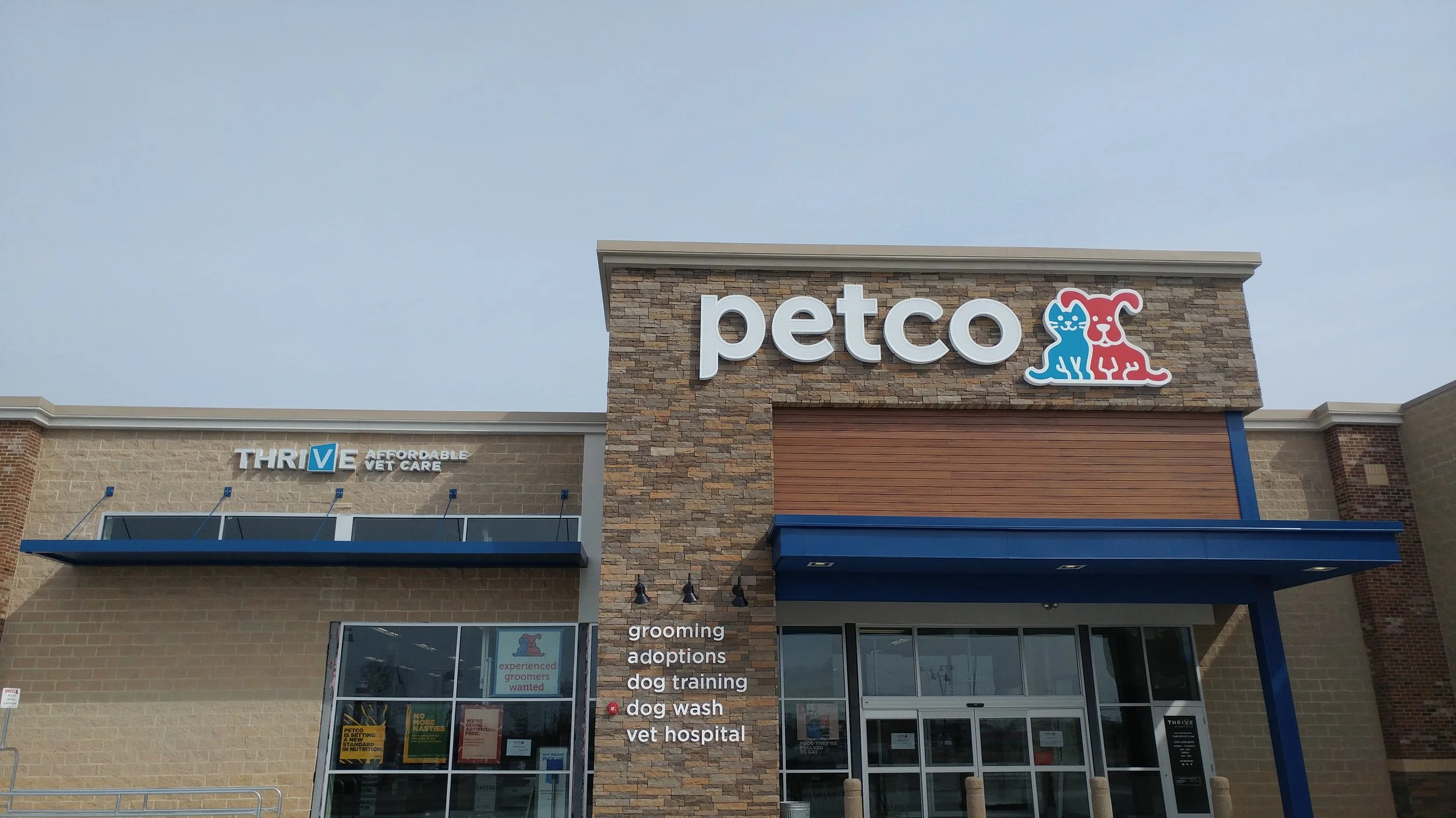 Exterior view of a Petco store with a sign featuring a blue cat and a red dog, and a list of services including grooming, adoptions, dog training, dog wash, and vet hospital.
