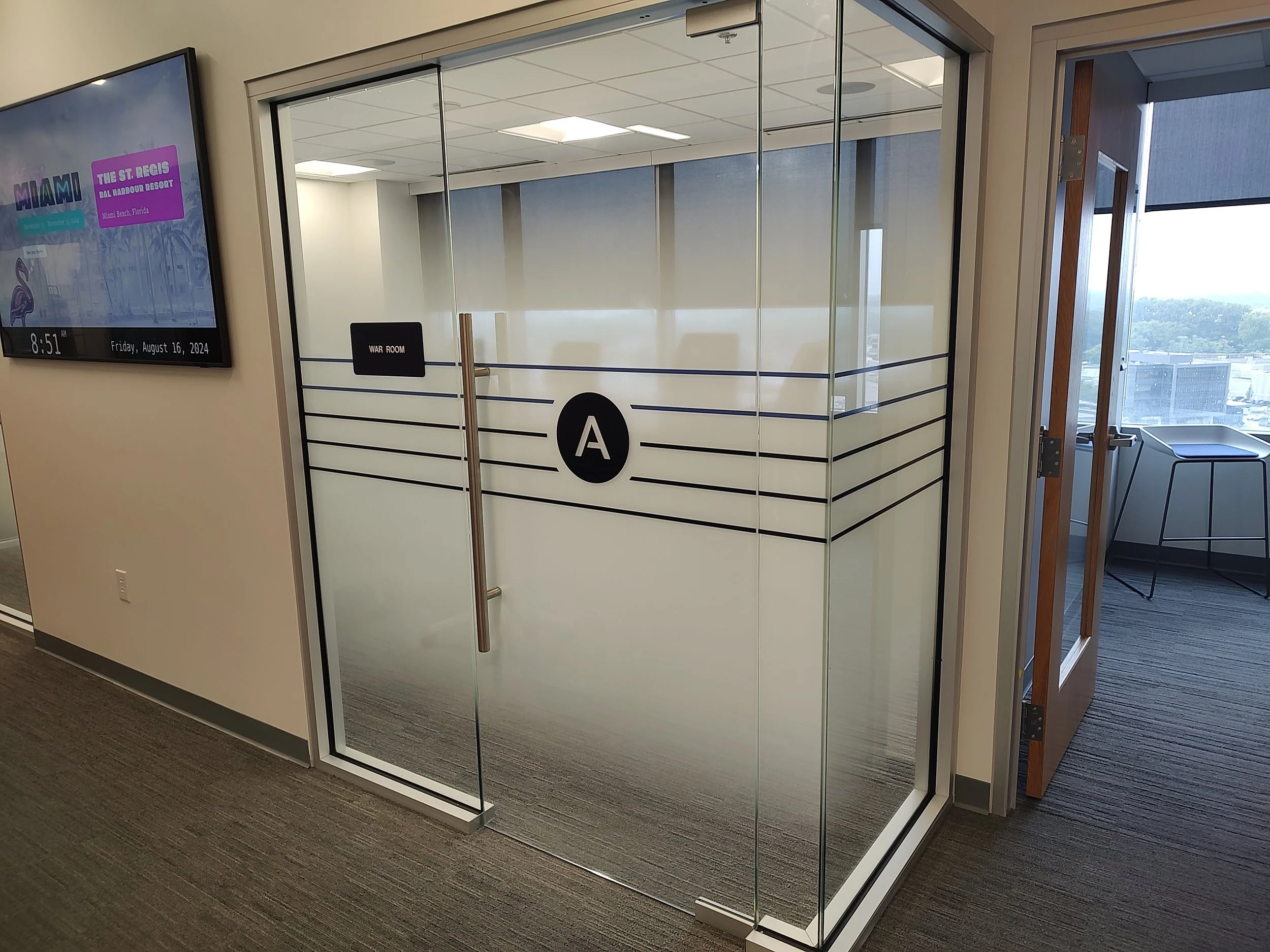 Glass door with black stripe design, labeled 'WAR ROOM' and marked 'A', in an office building, with a view of the city outside.