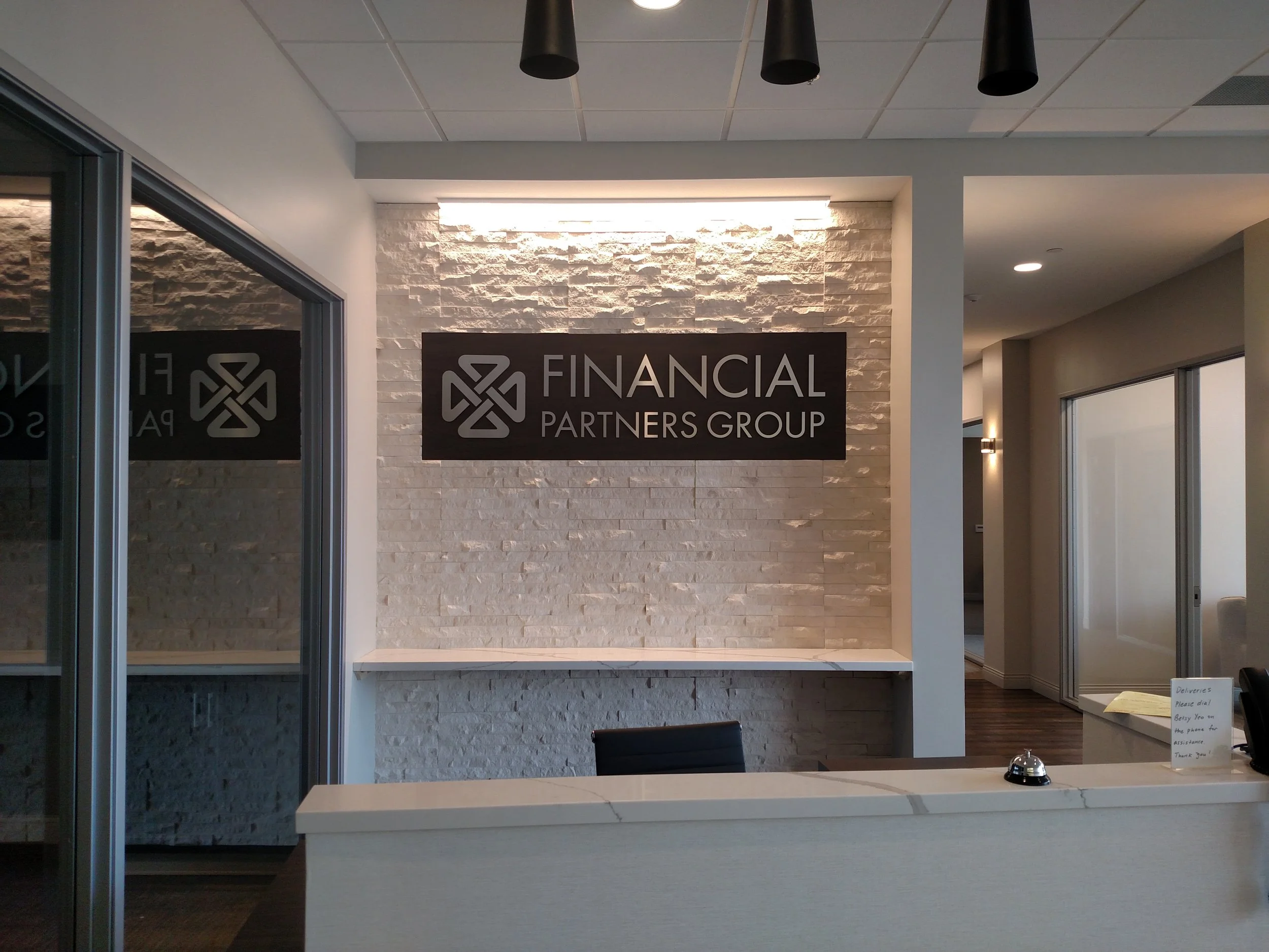 Reception area of a financial firm with a sign that reads 'Financial Partners Group' on a white brick wall.