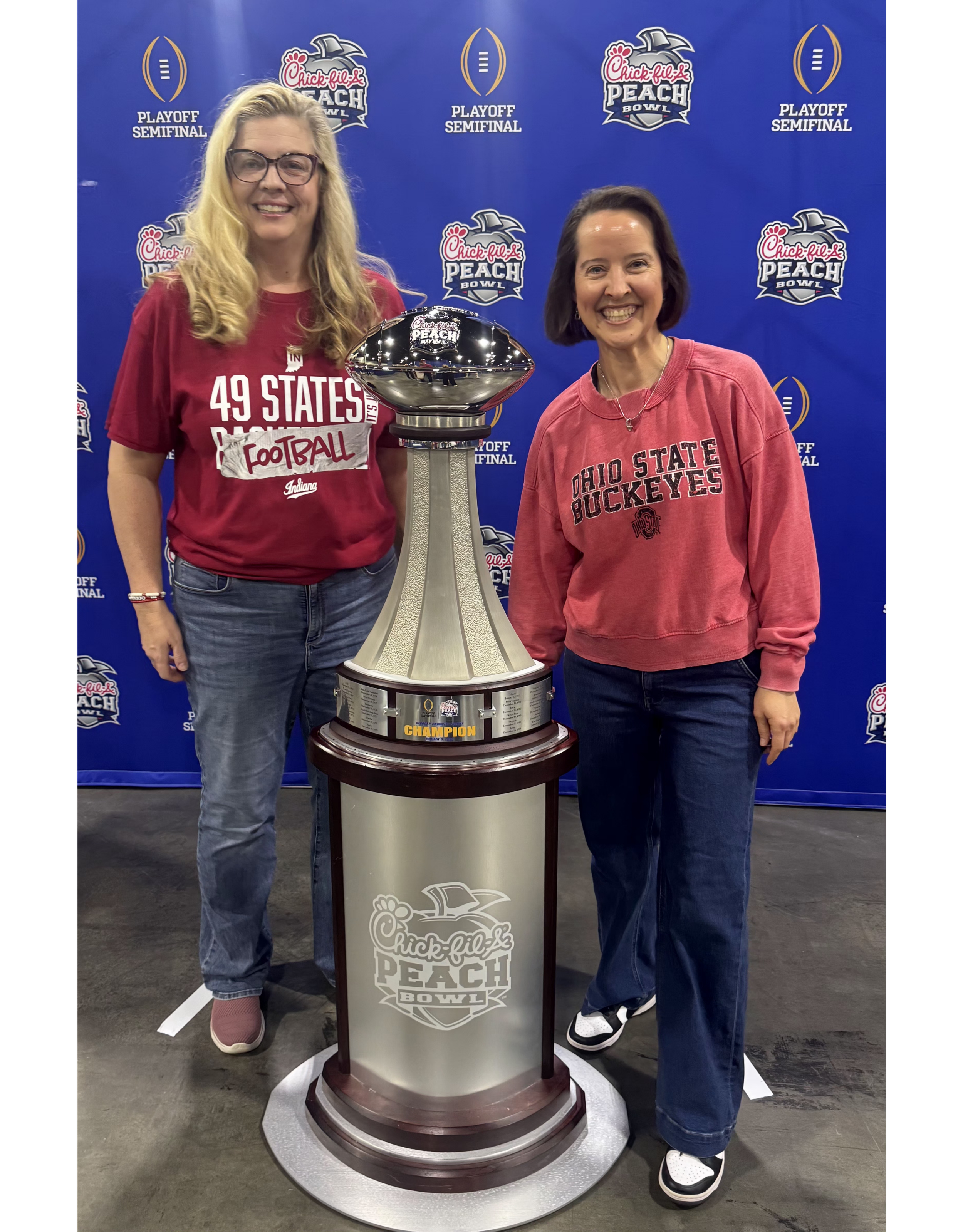 Beth and Jenny standing next to the College Football Playoff National Championship trophy at the Peach Bowl, smiling.