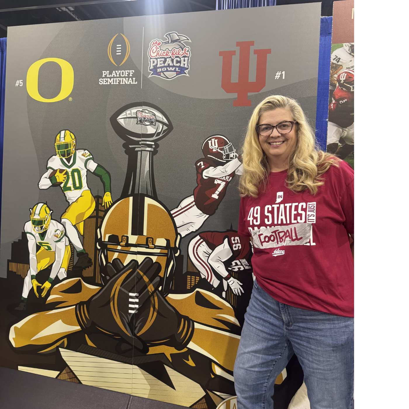 Beth standing in front of a large sports-themed mural. The mural features football players, a football helmet, and Championship Bowl logos for the Chick-fil-A Peach Bowl, with team logos including Indiana and Ohio State.