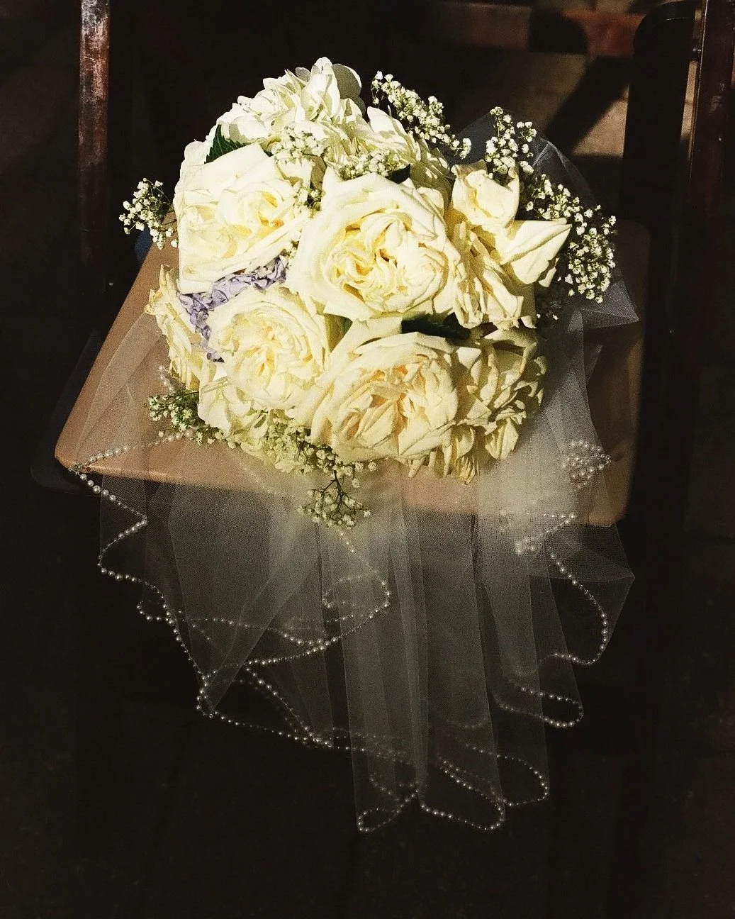 Bouquet of white roses and baby's breath on a table with a sheer, beaded tablecloth.