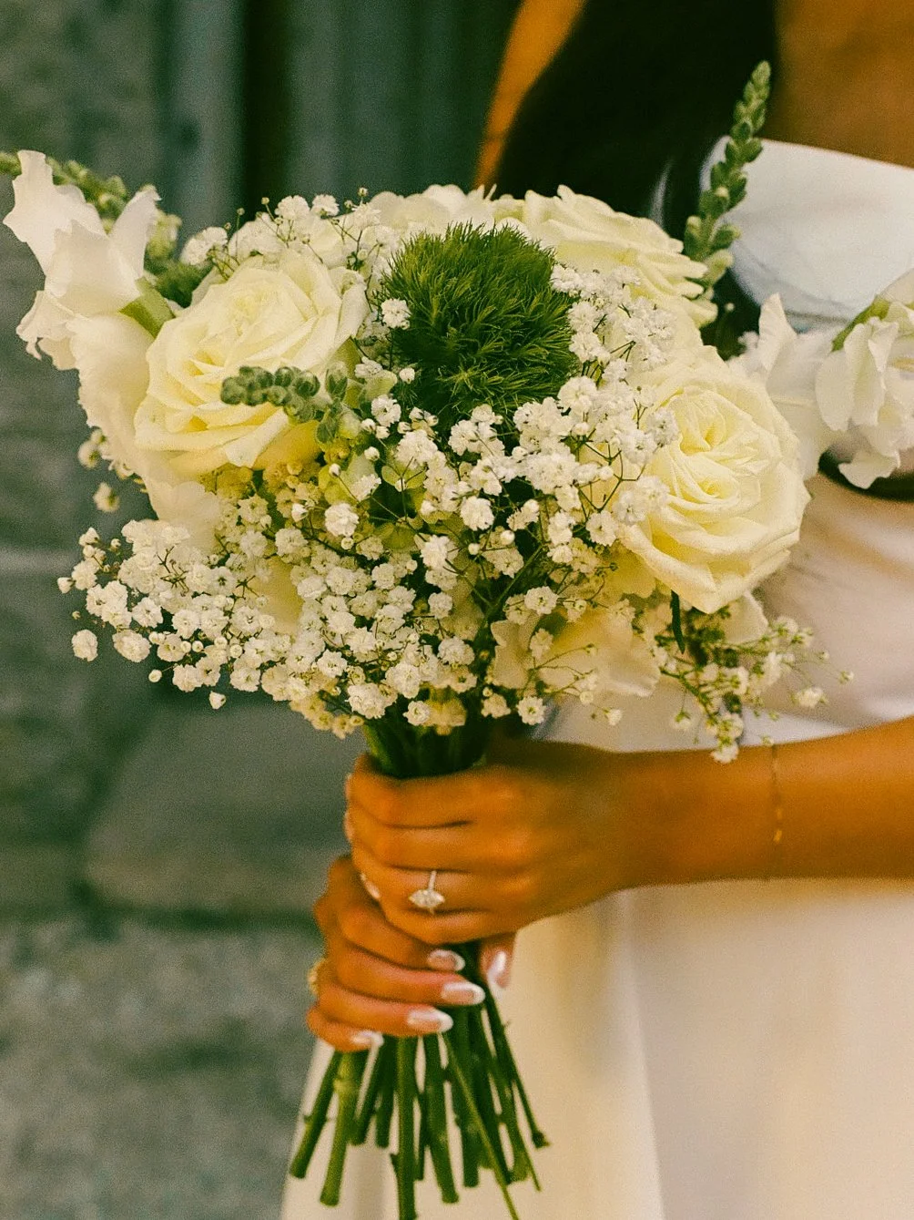 Close-up of a person holding a bouquet of white roses, baby's breath, and greenery at a wedding.