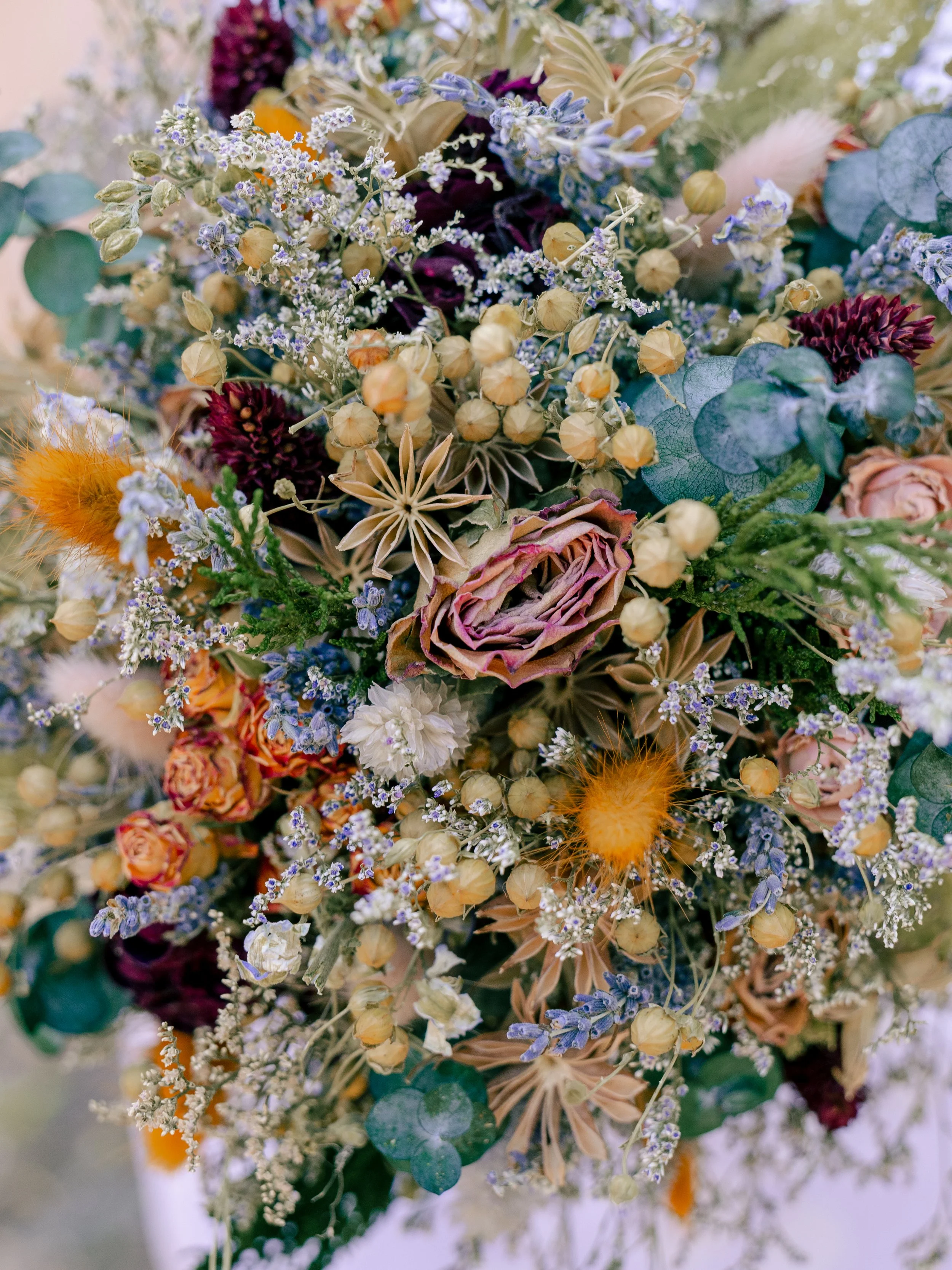 Close-up of a colorful bouquet of flowers including purple, white, and orange blooms, with green leaves and dried elements.