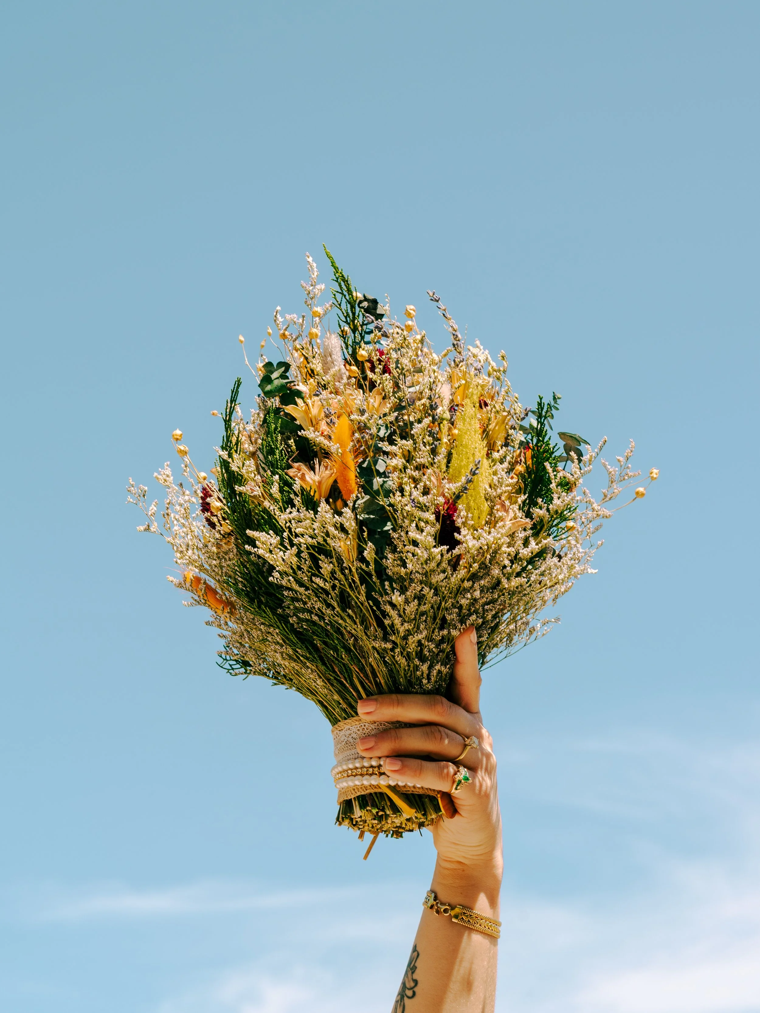 Hand holding a bouquet of wildflowers against a clear blue sky.