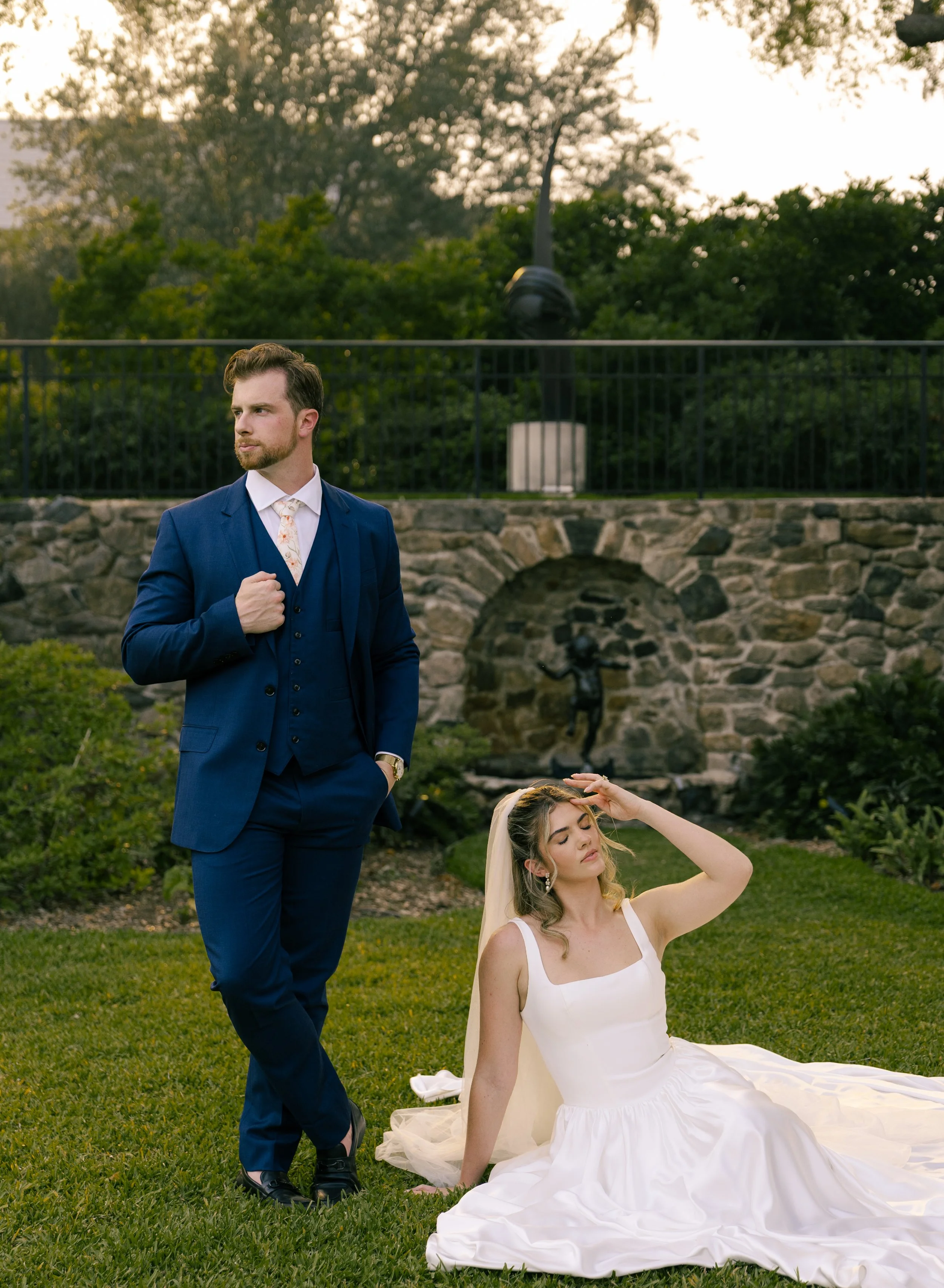 A couple poses editorially for wedding portraits at the Cummer Museum & Gardens in Jacksonville, Florida. The groom wears a navy blue suit and the bride wears a dress from Love, a Bridal Boutique in Jacksonville Beach, Florida.