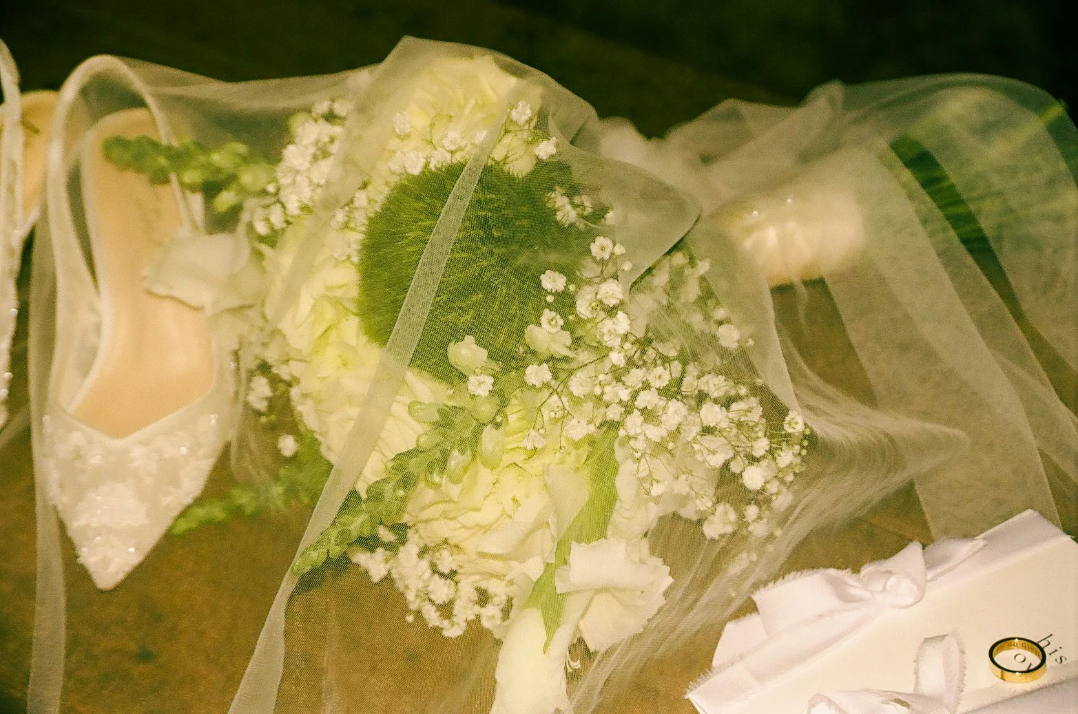 A bridal bouquet with white roses, baby's breath, and greenery, wrapped in transparent tulle with white ribbons.