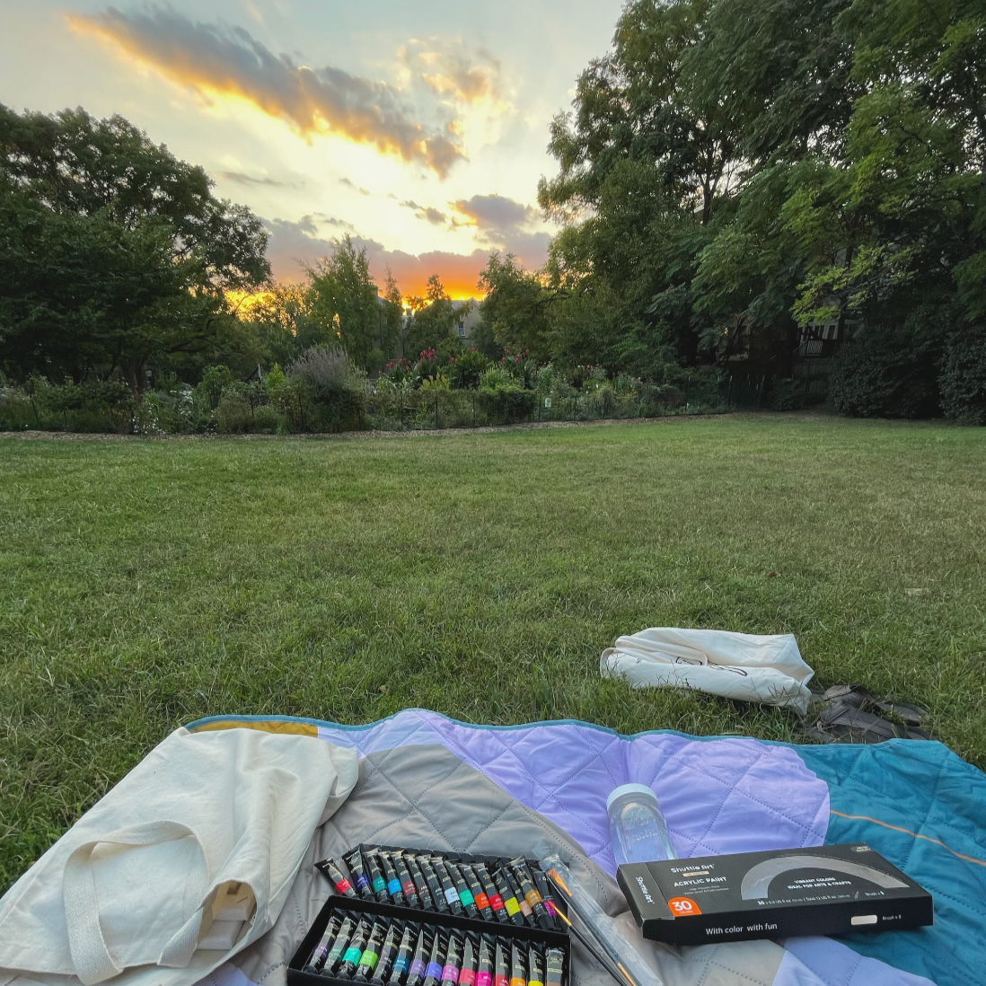 Outdoor craft retreat concept. Picnic blanket in the grass with art supplies. Sunset in the background, a beautiful location for creating