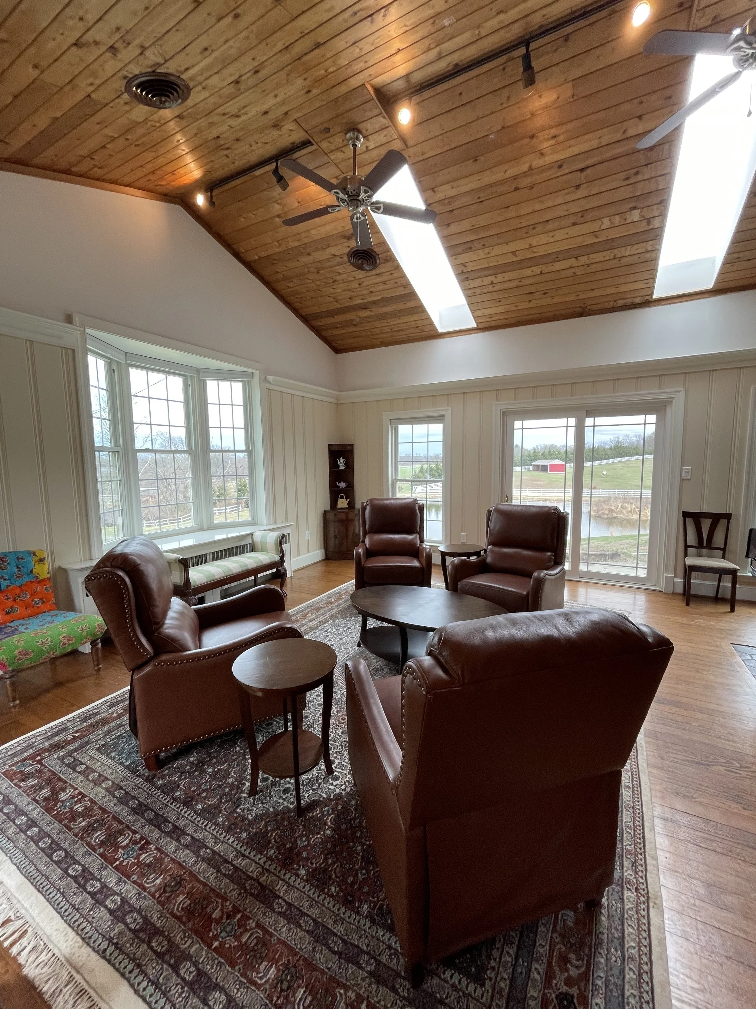 Cozy craft retreat location. Living room with leather chairs, windows, ceiling fans, skylights, wooden floor and ceiling, and a view outside.