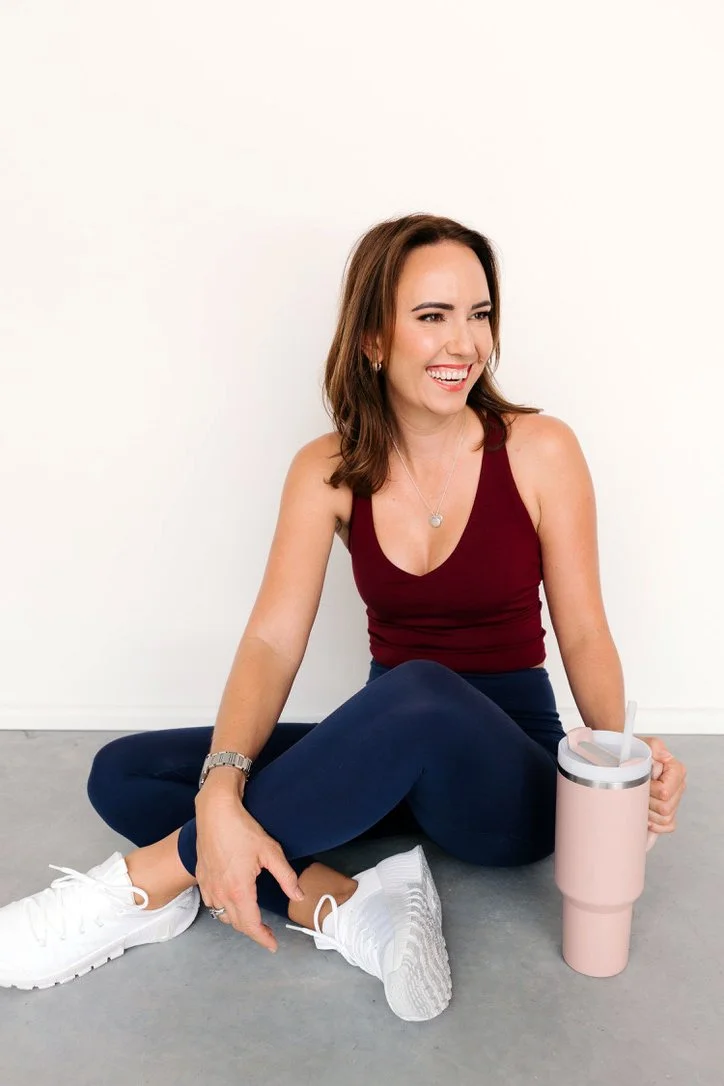 Cailie Ford laughing while sitting on the floor in activewear with a water bottle
