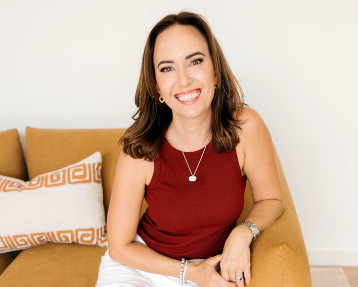 Cailie Ford smiling, sitting on a mustard sofa in a bright living room