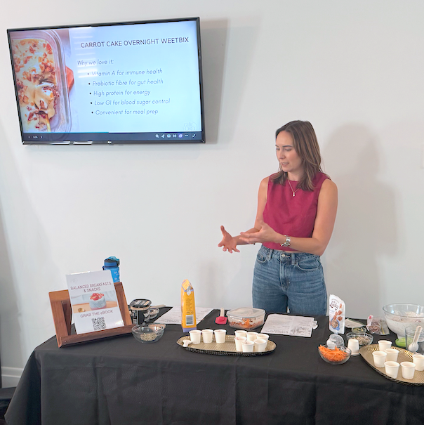 Cailie Ford presenting a cooking demonstration workshop, with a carrot cake overnight weetbix recipe slide displayed on screen