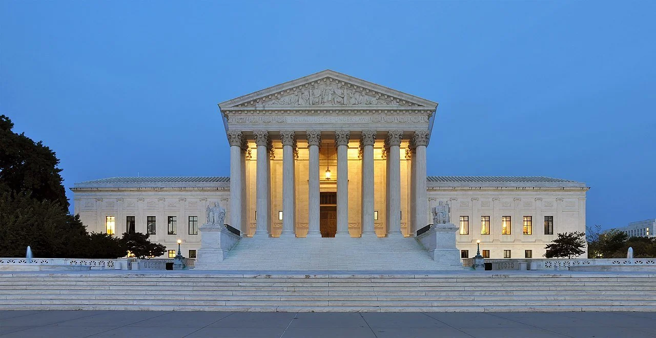 The United States Supreme Court building at dusk, with illuminated columns and classical architecture.