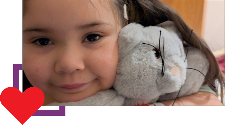 A young girl holding a gray stuffed animal with glasses close to her face.