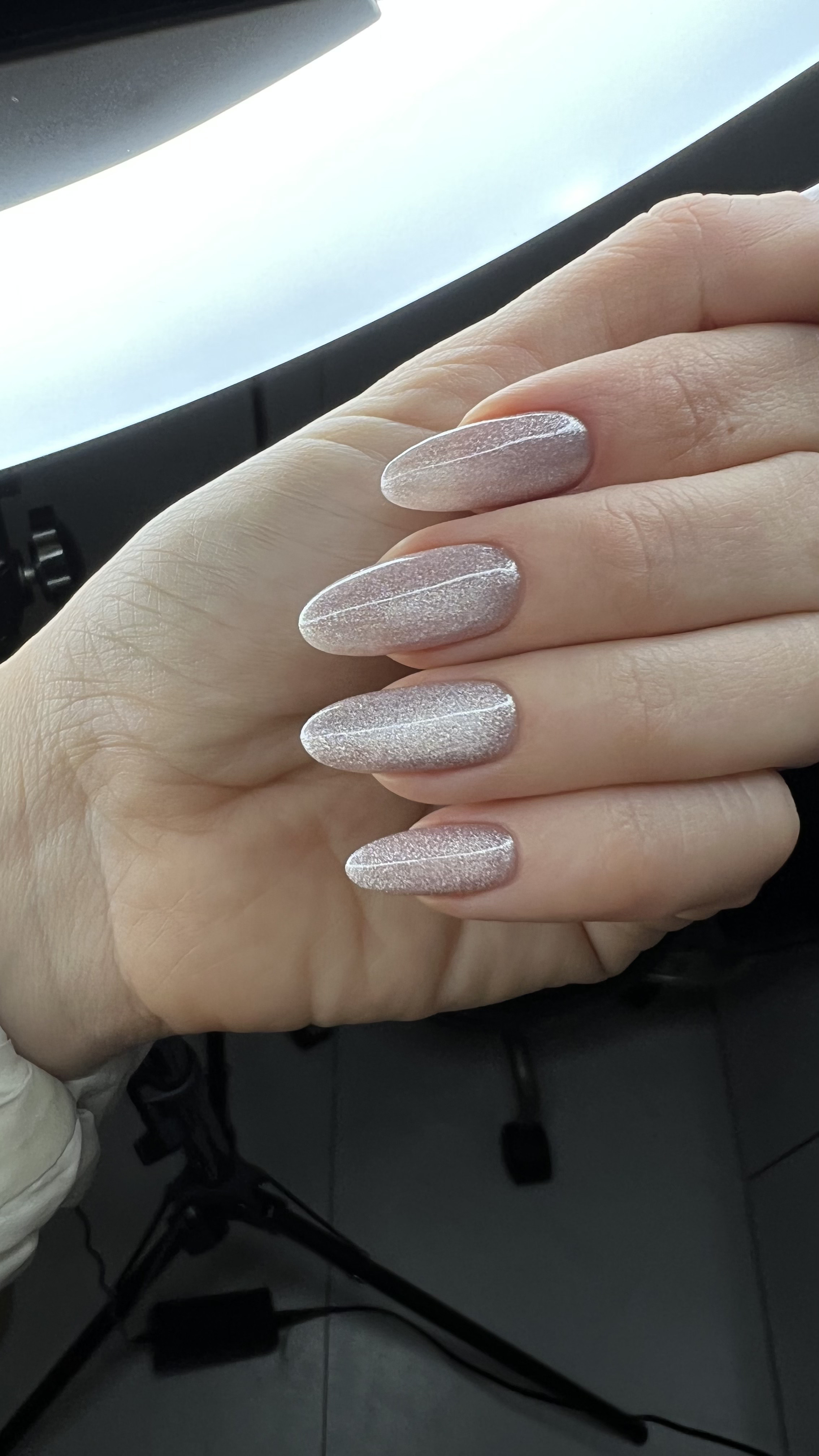 Hand with long, oval-shaped nails painted with glittery, nude-colored nail polish.