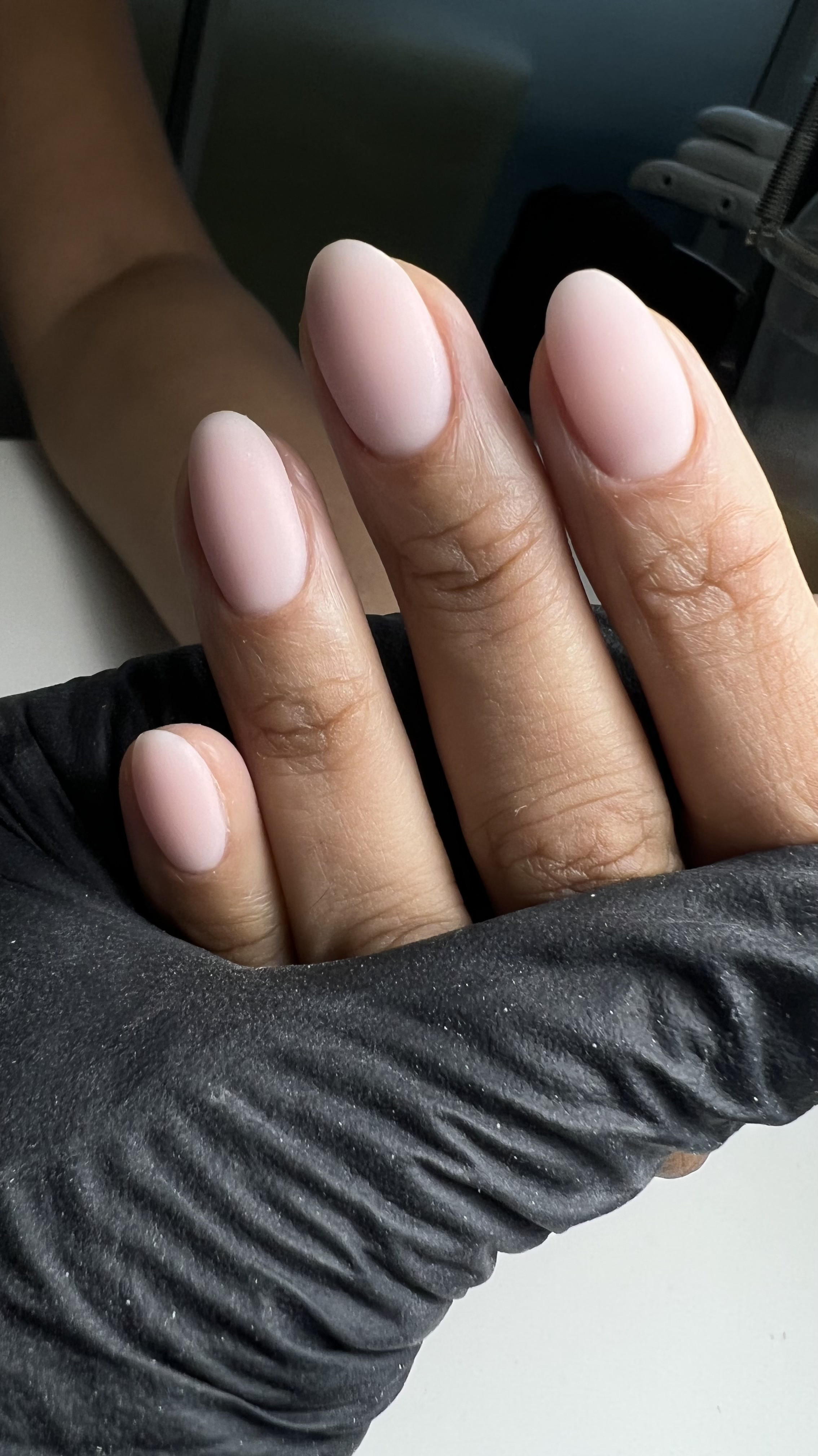 Close-up of a hand with well-manicured, pale pink nails resting on a black textured surface.