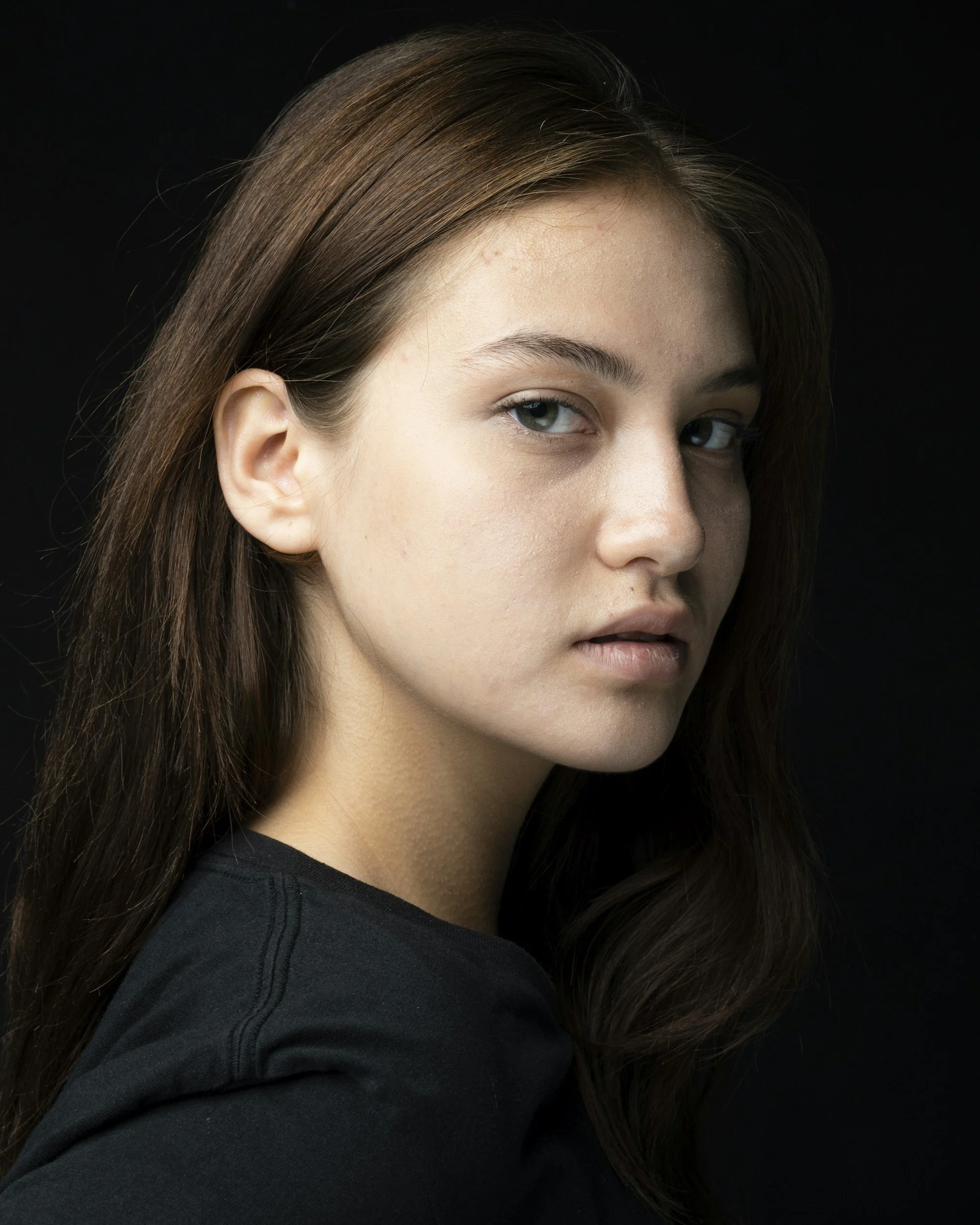 Close-up portrait of a young woman with brown hair and blue eyes against a black background.