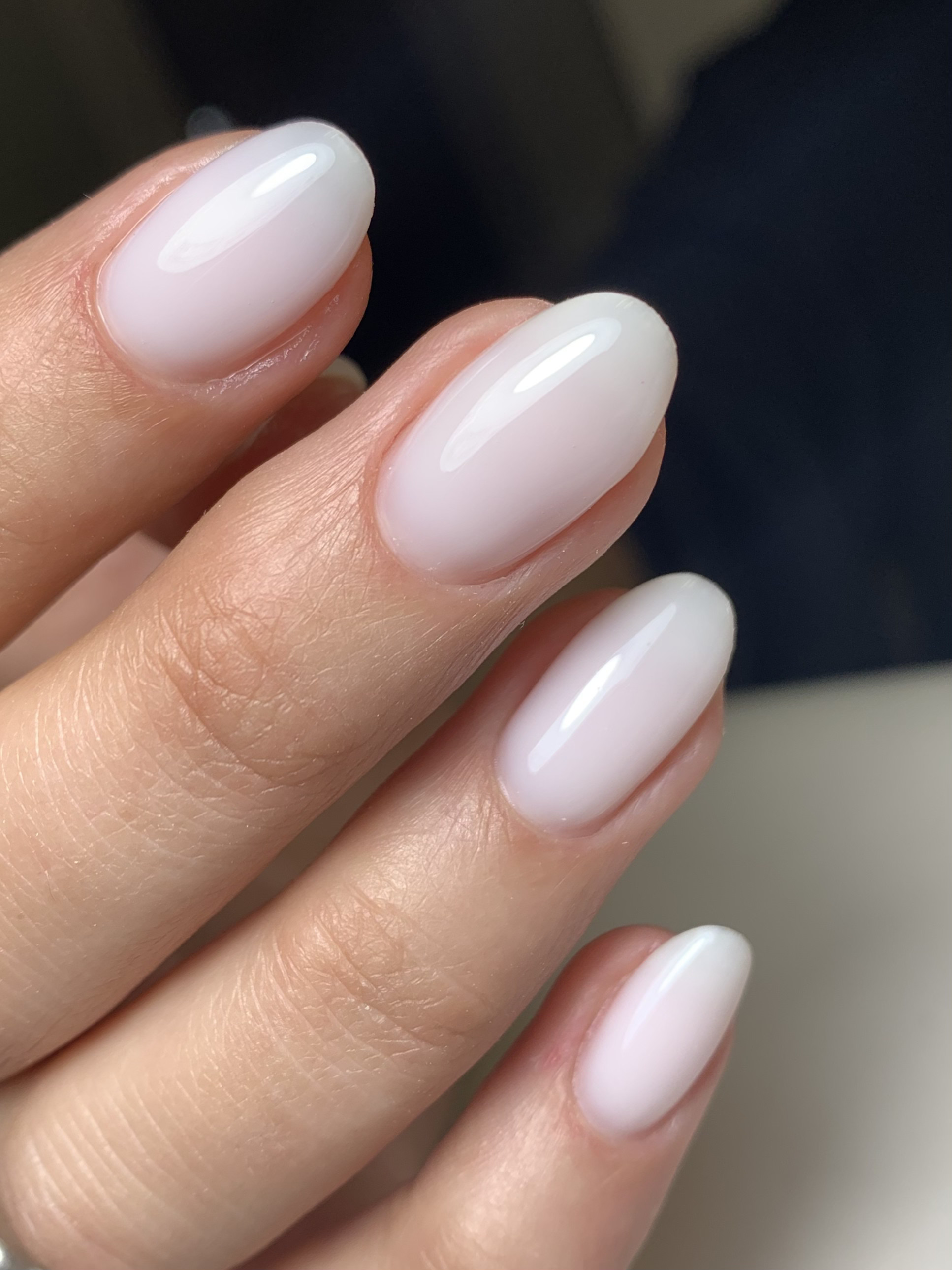 Close-up of a hand with neatly manicured oval nails painted in a glossy, pale pink or nude color.